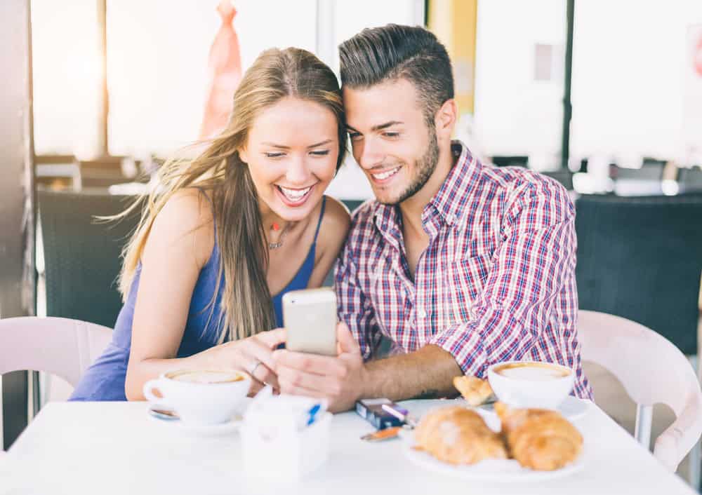 A happy couple in a coffee shop looking at pictures in a phone