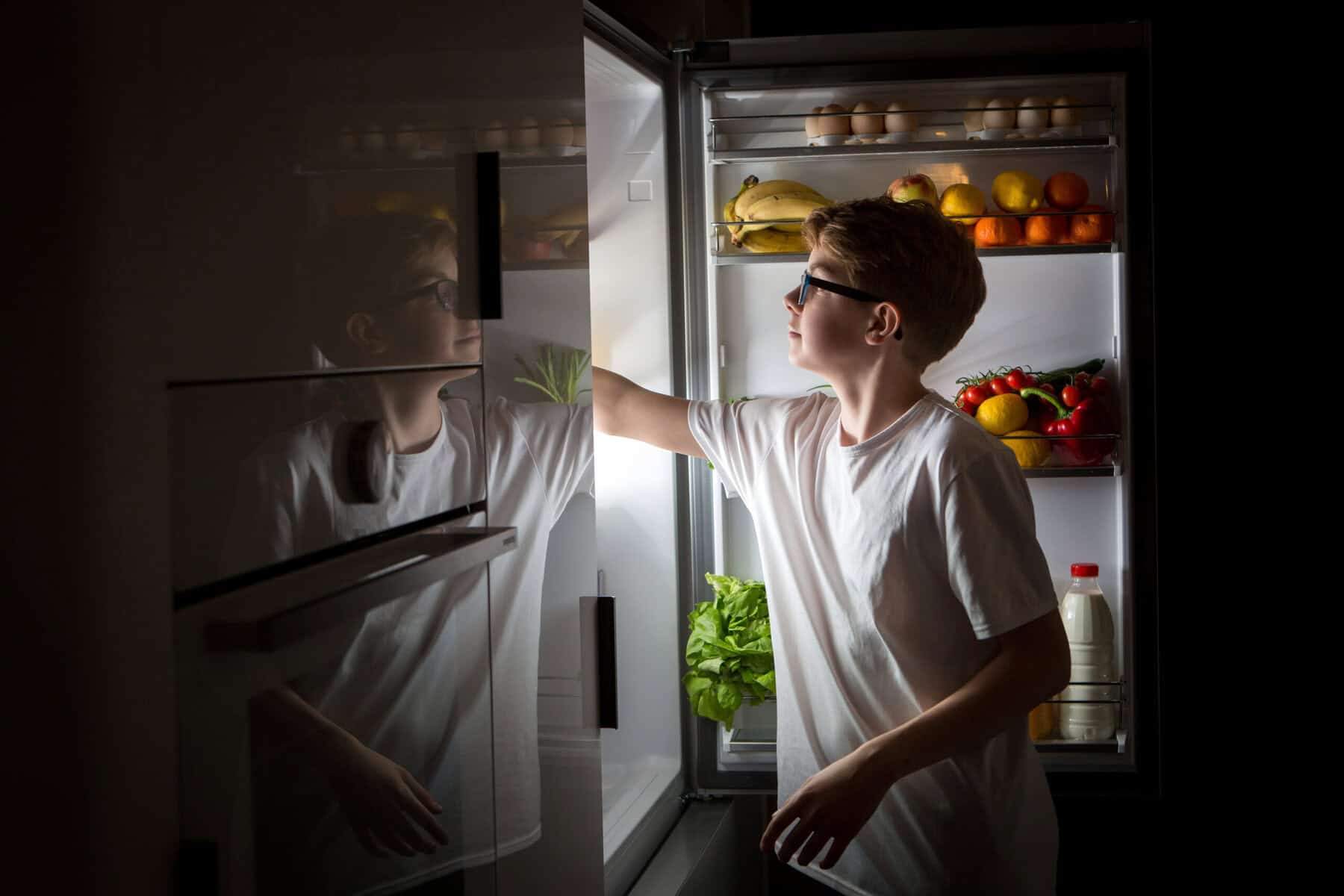 A boy looking in the refrigerator for a late nate snack.