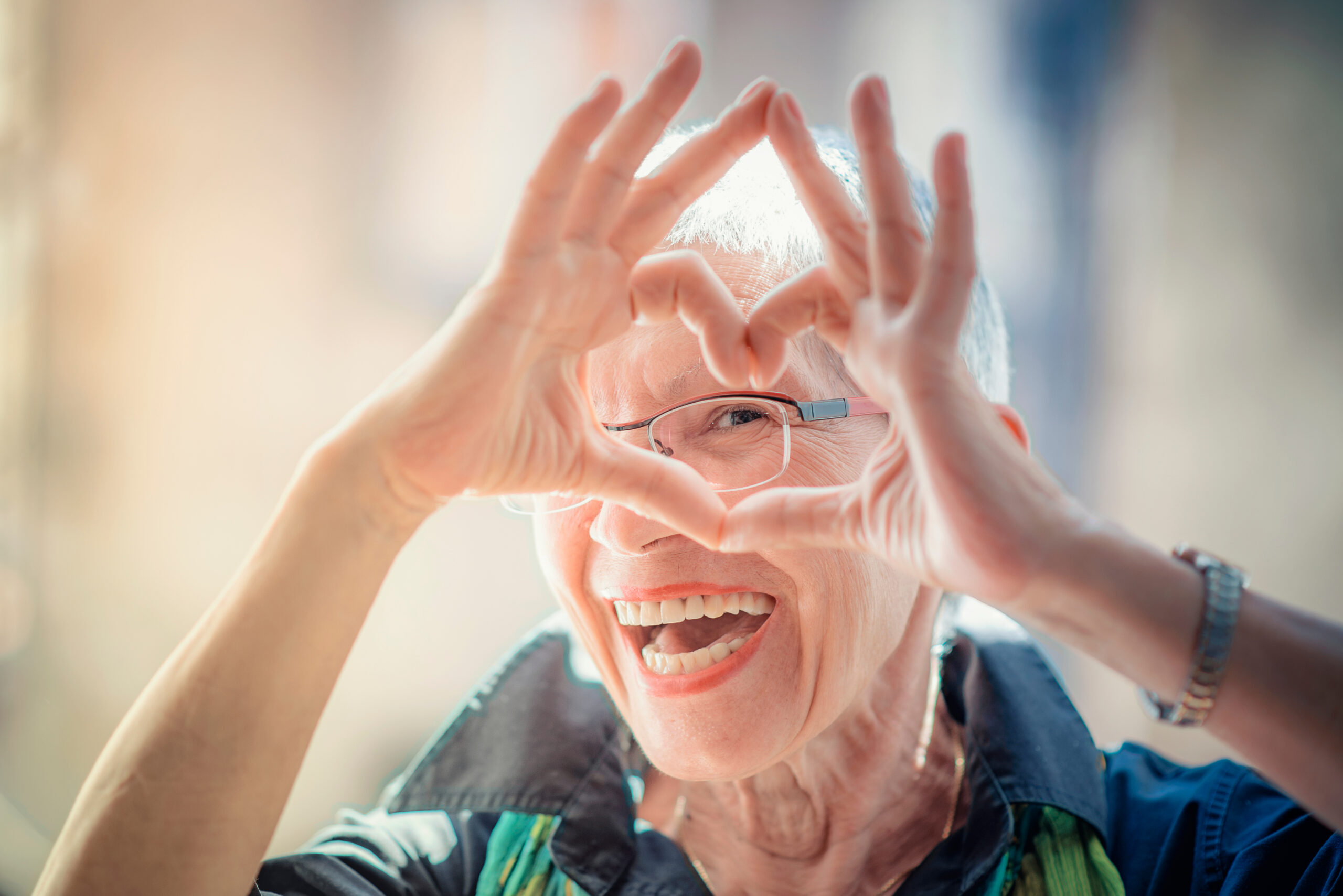 Senior woman making a heart shape with her hands and fingers while smiling.