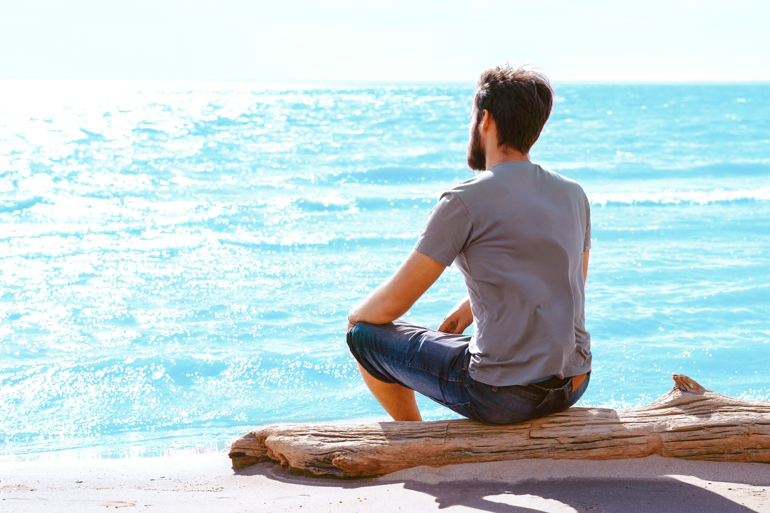 A man sitting alone on the beach while looking out at the ocean.