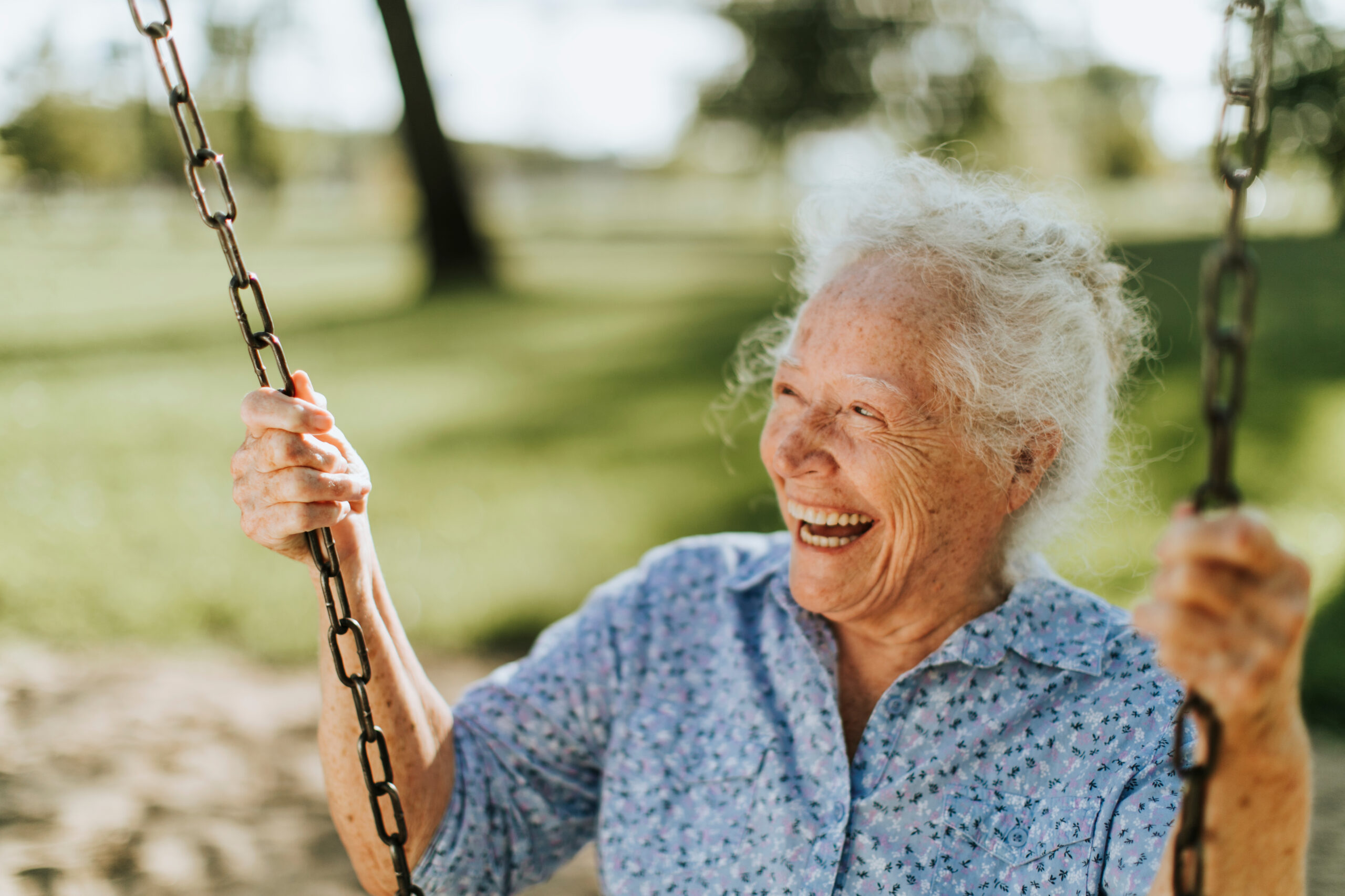 Cheerful senior woman on a swing at a playground.