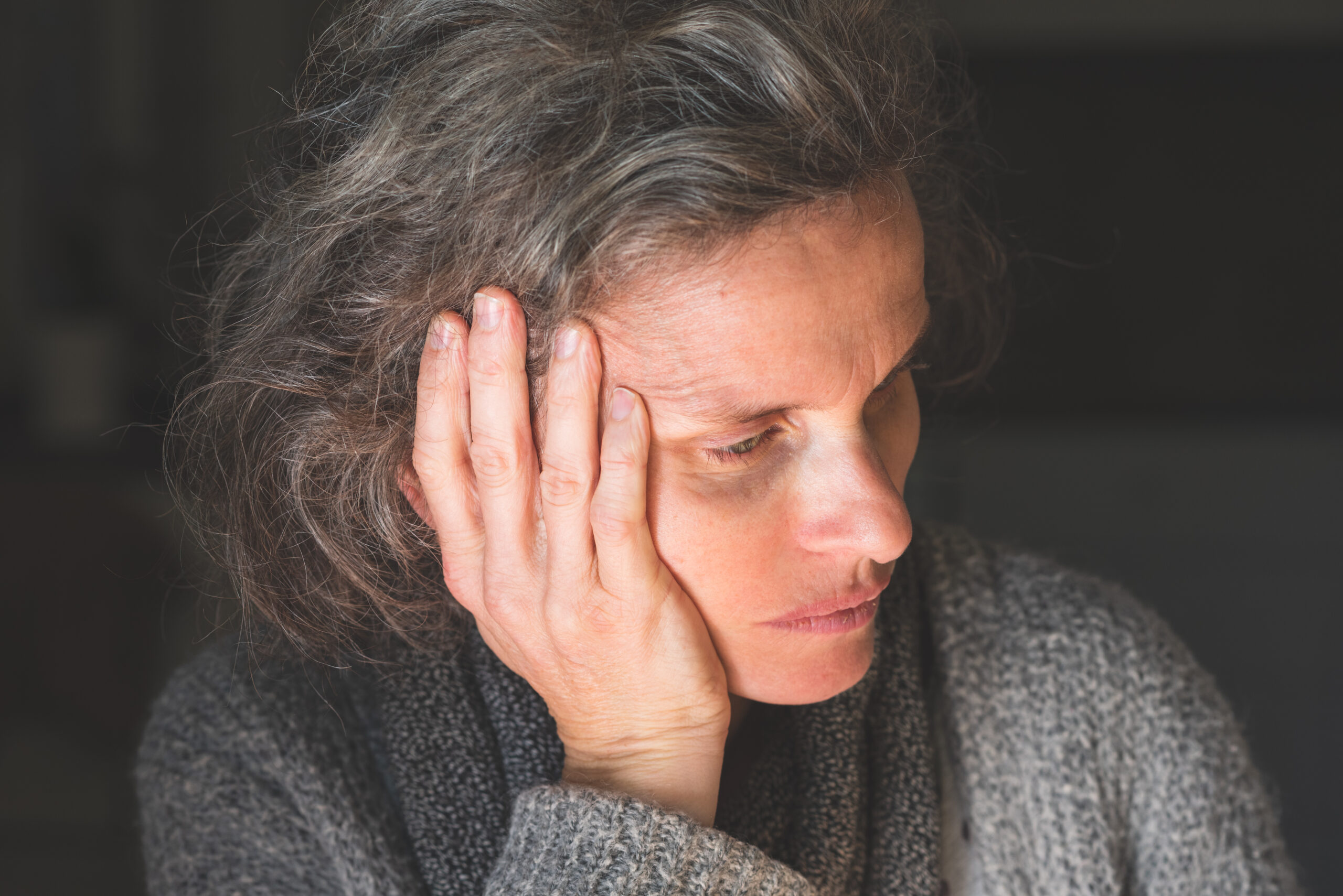 A middle aged woman with grey hair sitting in the dark.
