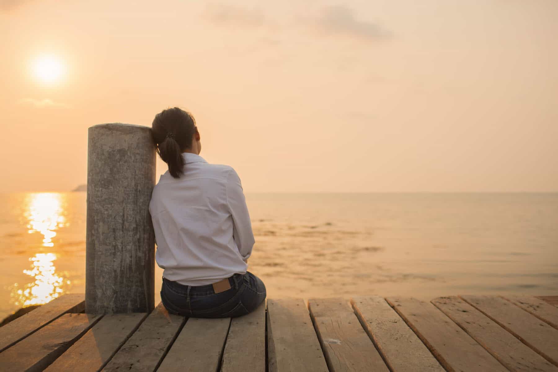 Woman sitting alone on pier at sunset.