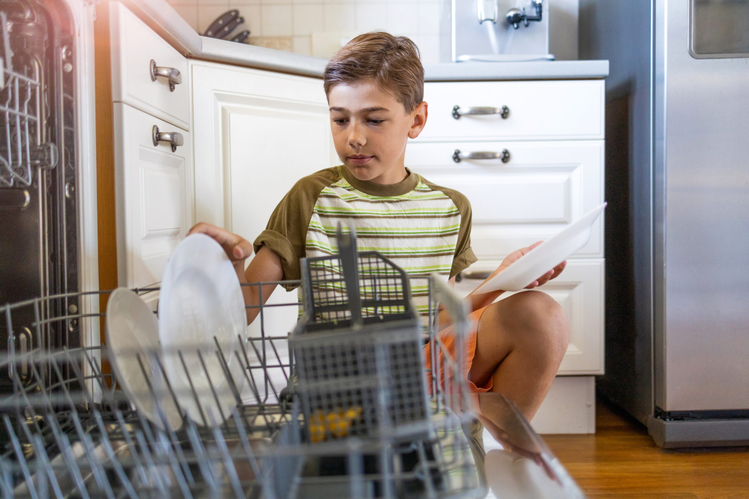 A young boy loading the dishwasher.