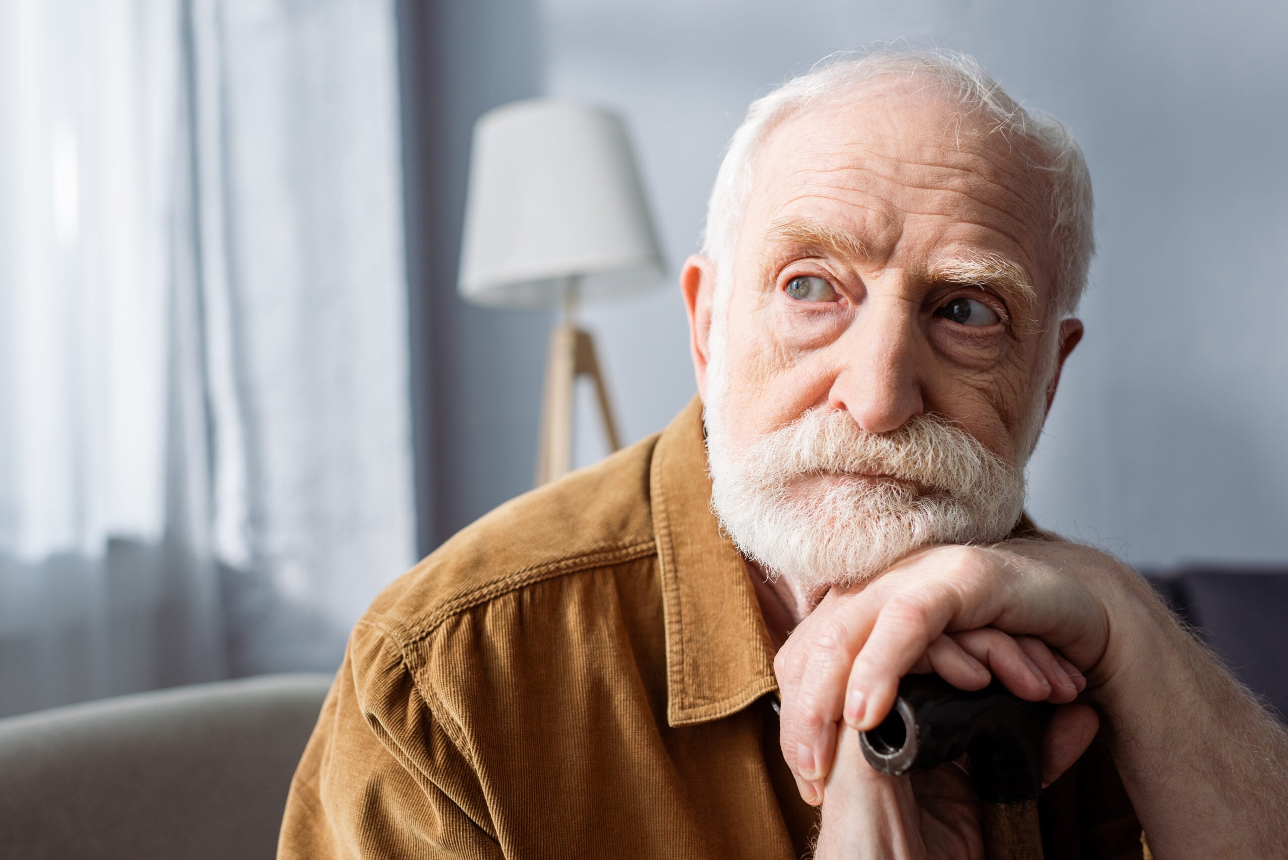 A lonely senior man looking away and leaning on his walking stick.
