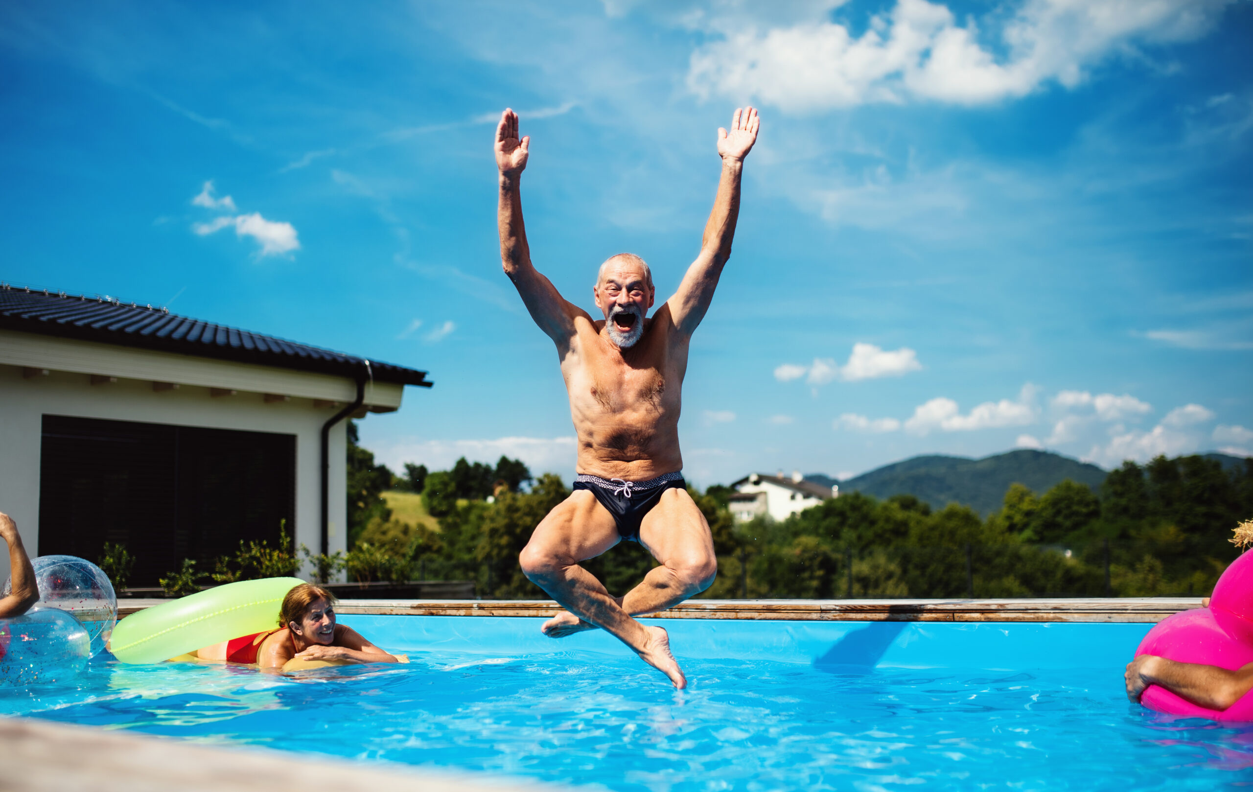 A group of cheerful seniors in a backyard swimming pool.