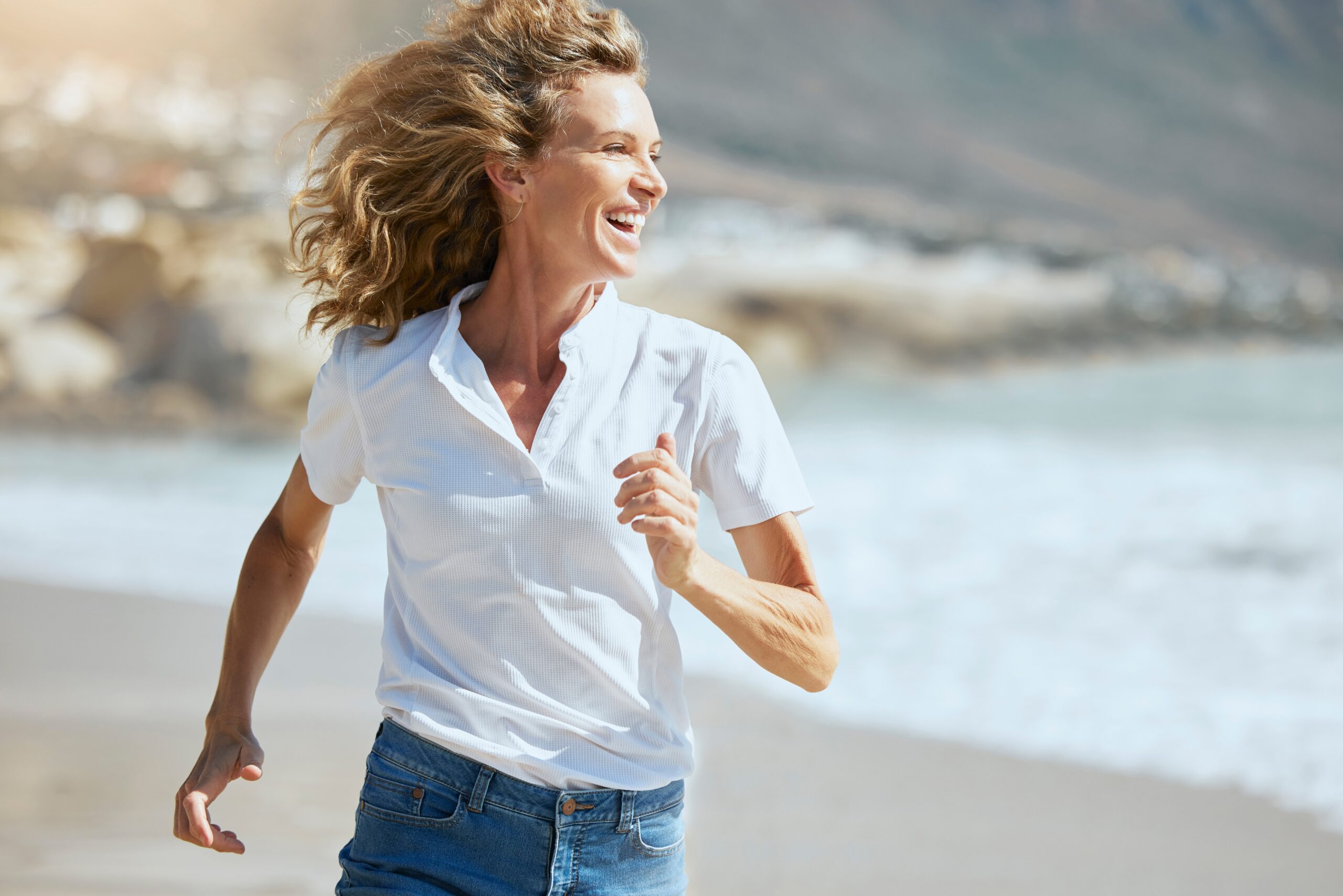 Cheerful mature woman running on the beach on a sunny day.