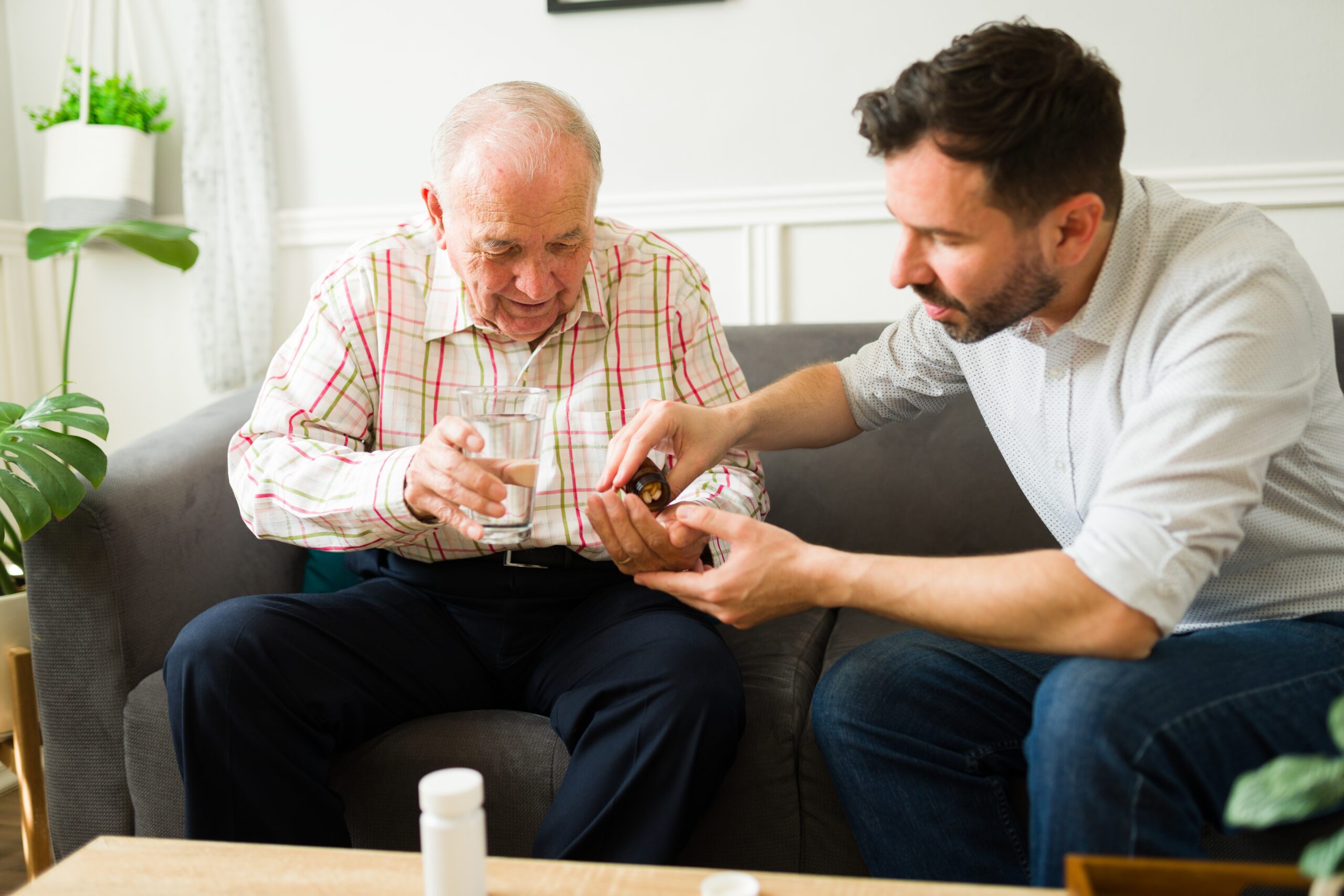 Adult son giving his elderly father with health problems his medicine.
