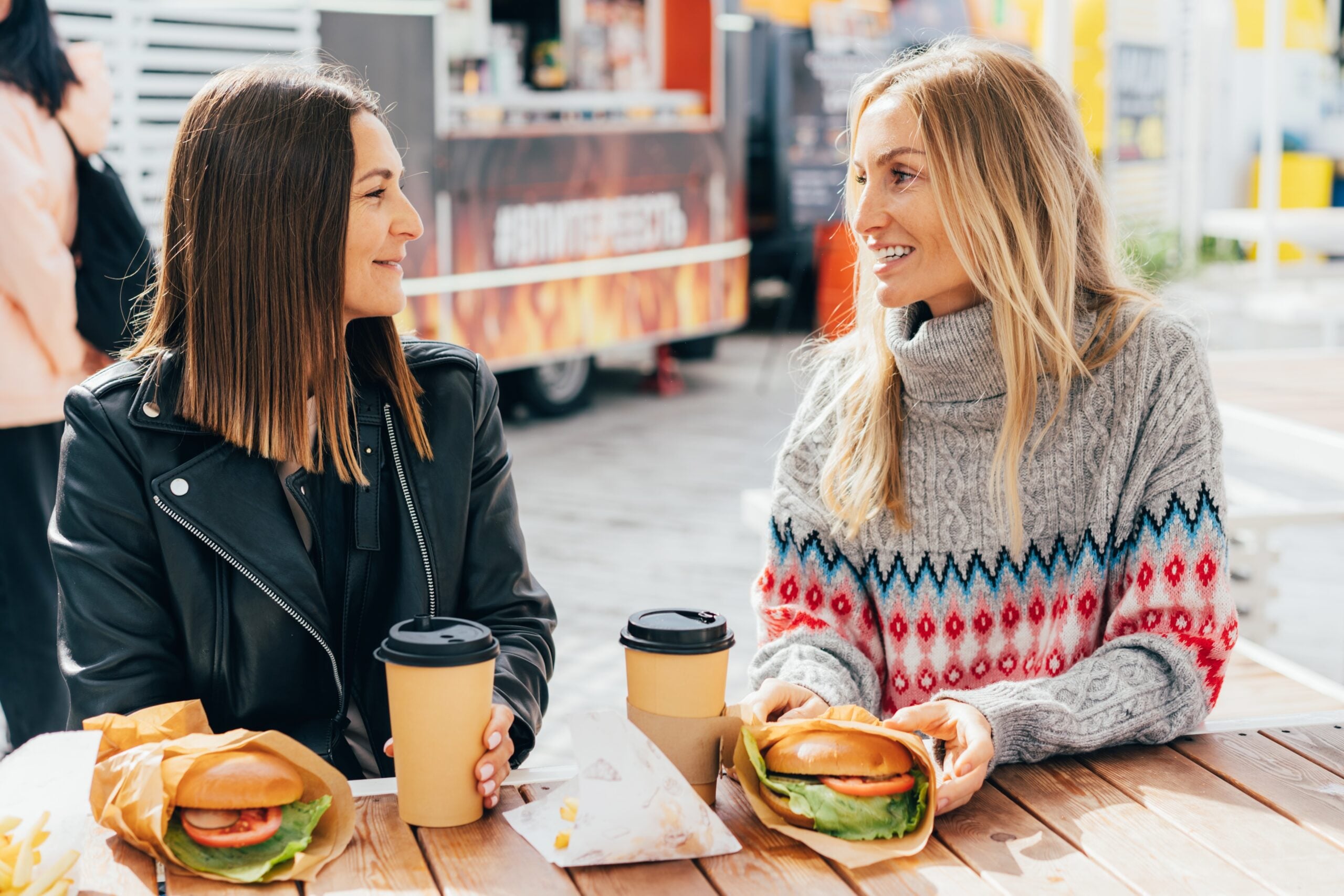 Two female friends eating burgers at a street market.