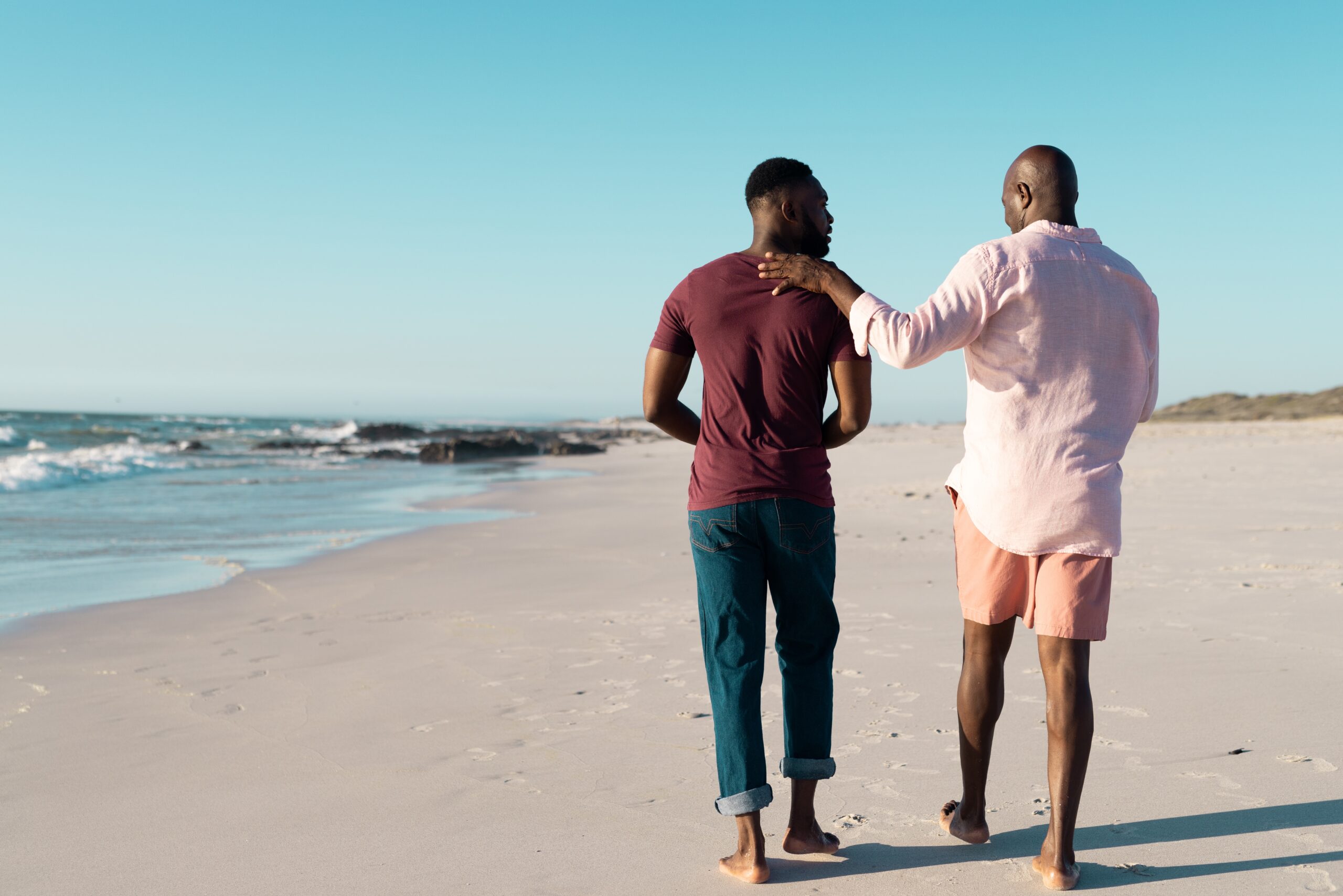 A senior father with his adult son on a beach walk.