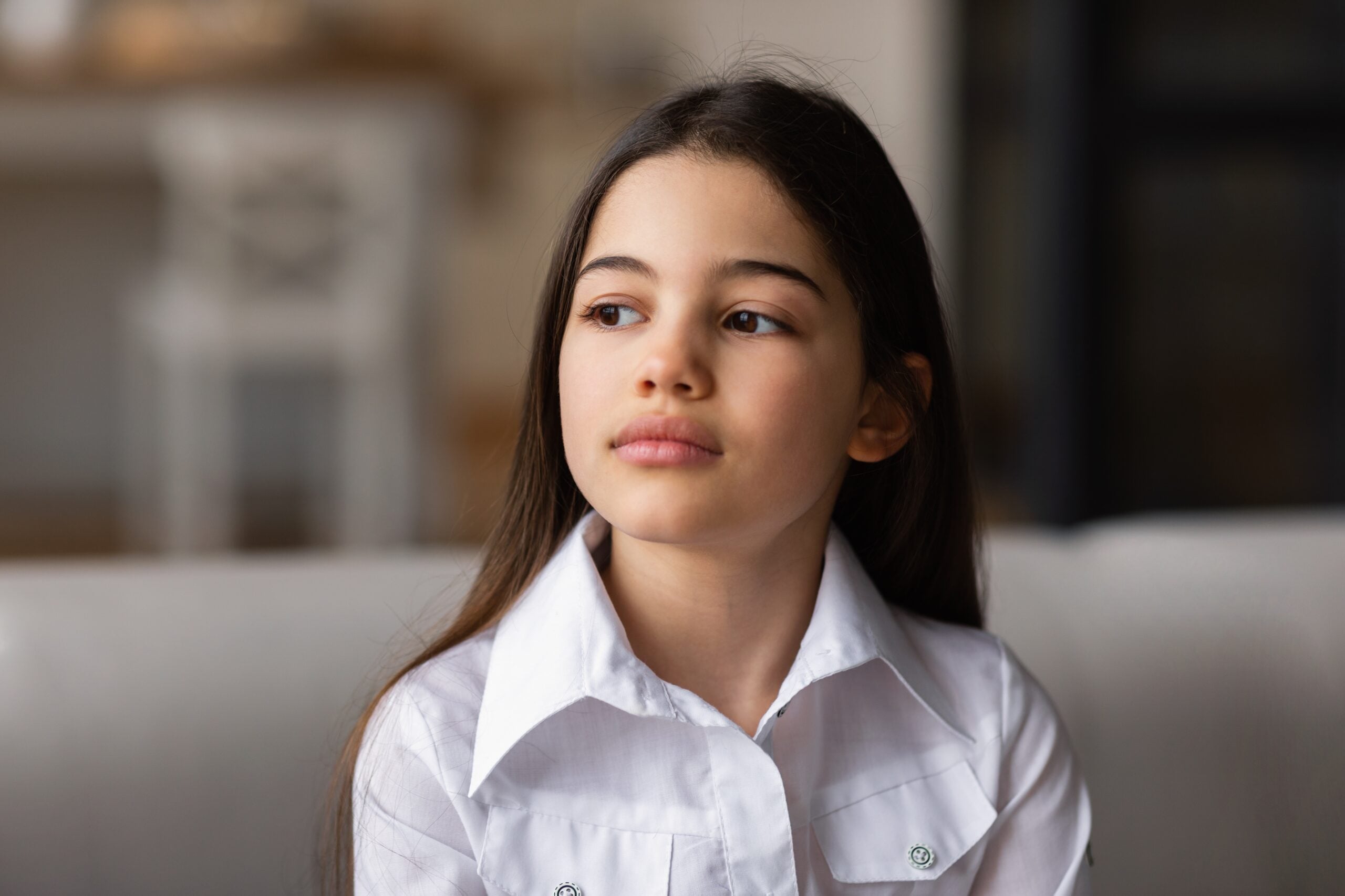 An upset preteen girl sitting alone on sofa at home.
