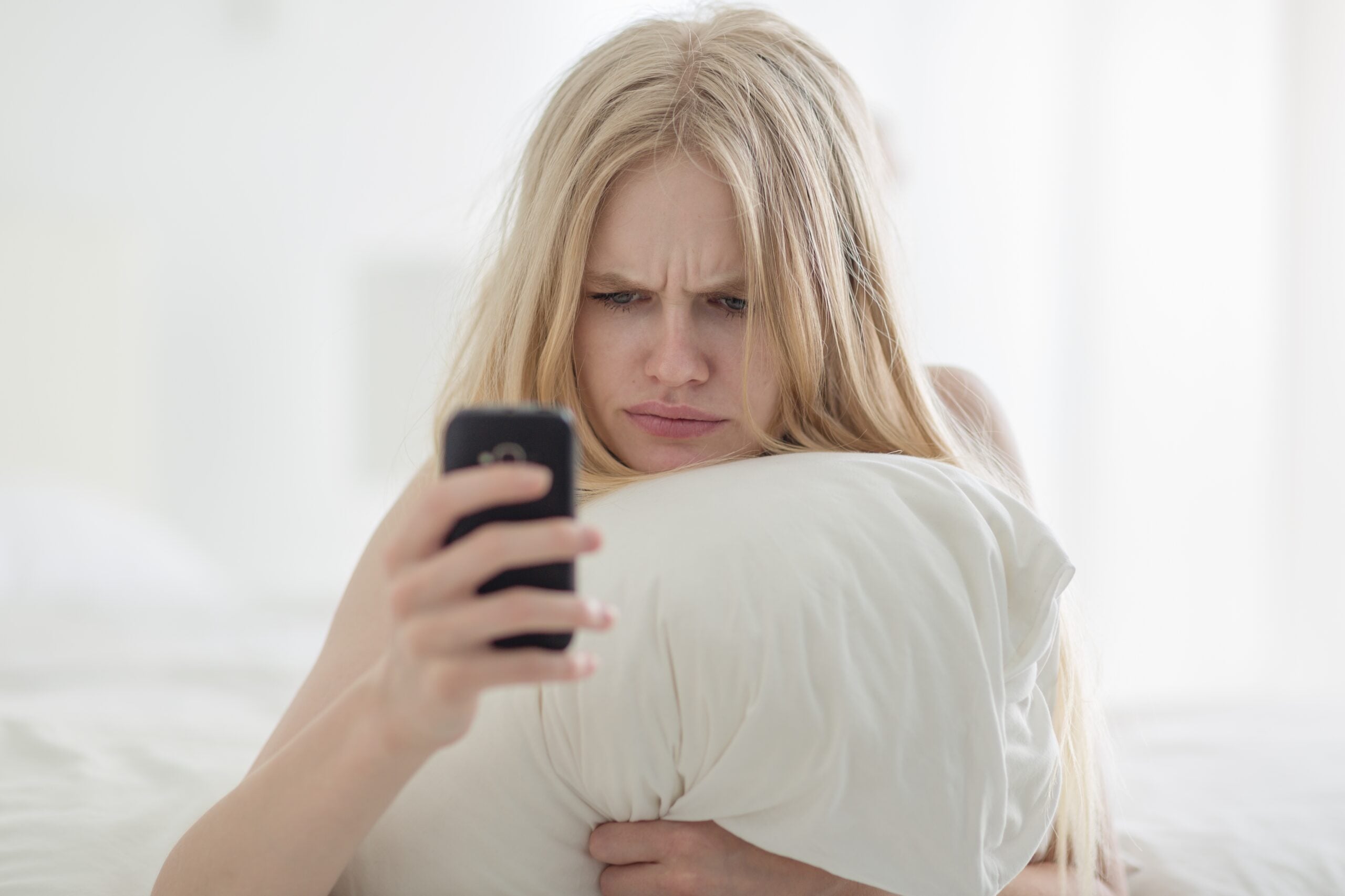 Upset woman holding her phone while lying in bed.