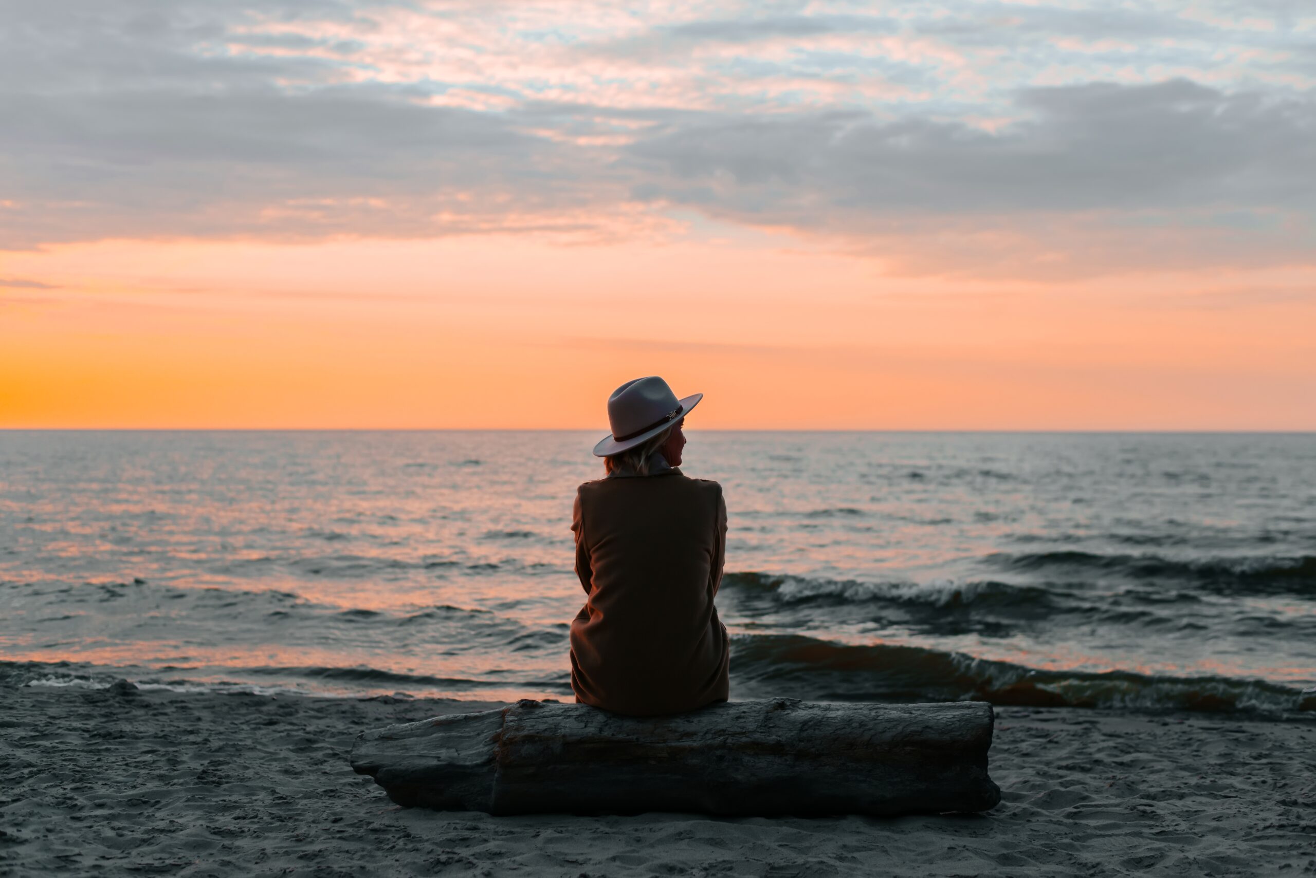 Woman sitting alone on a log looking out at the bay.