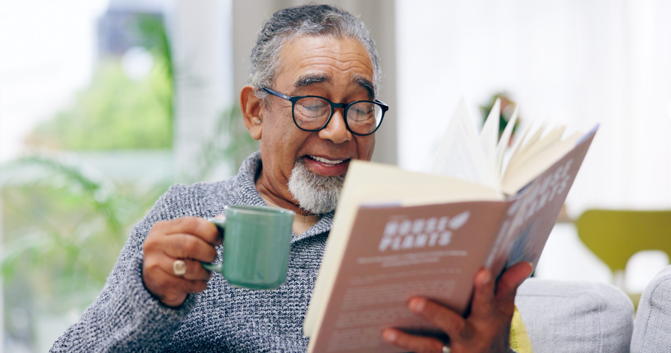 A senior man with his book and a coffee on the sofa.