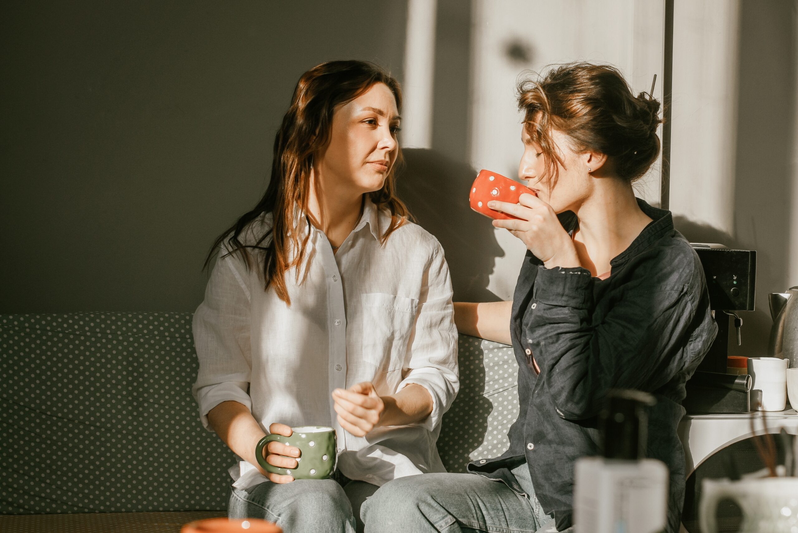 Two female friends enjoying morning coffee in a cozy home kitchen.