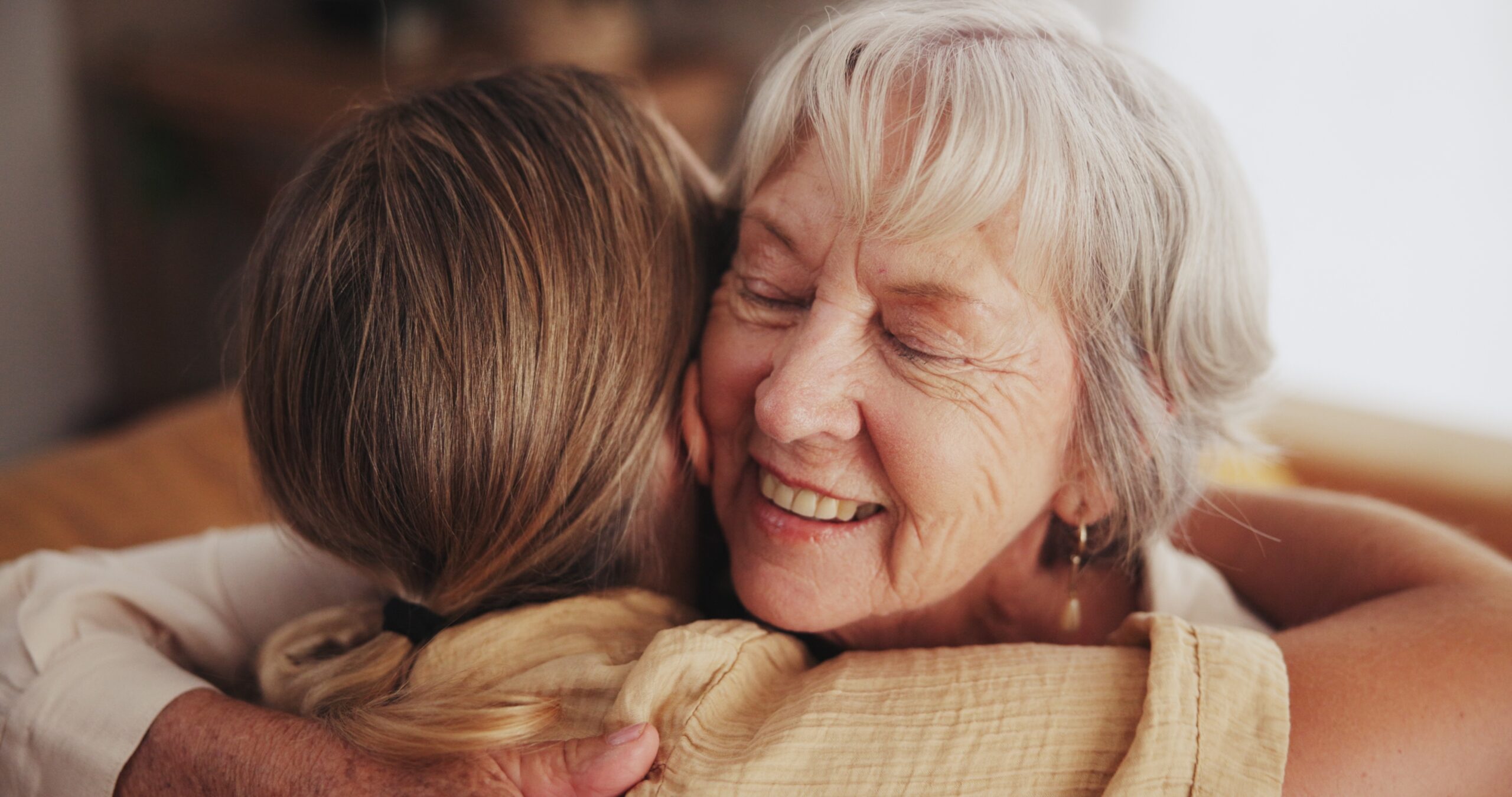 A senior woman getting a hug and visit from her adult daughter.