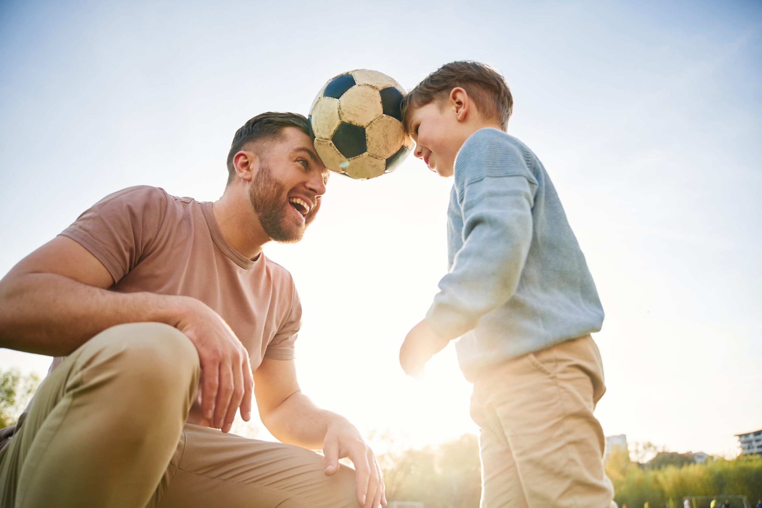 Happy father with his son on the soccer field at sunset.