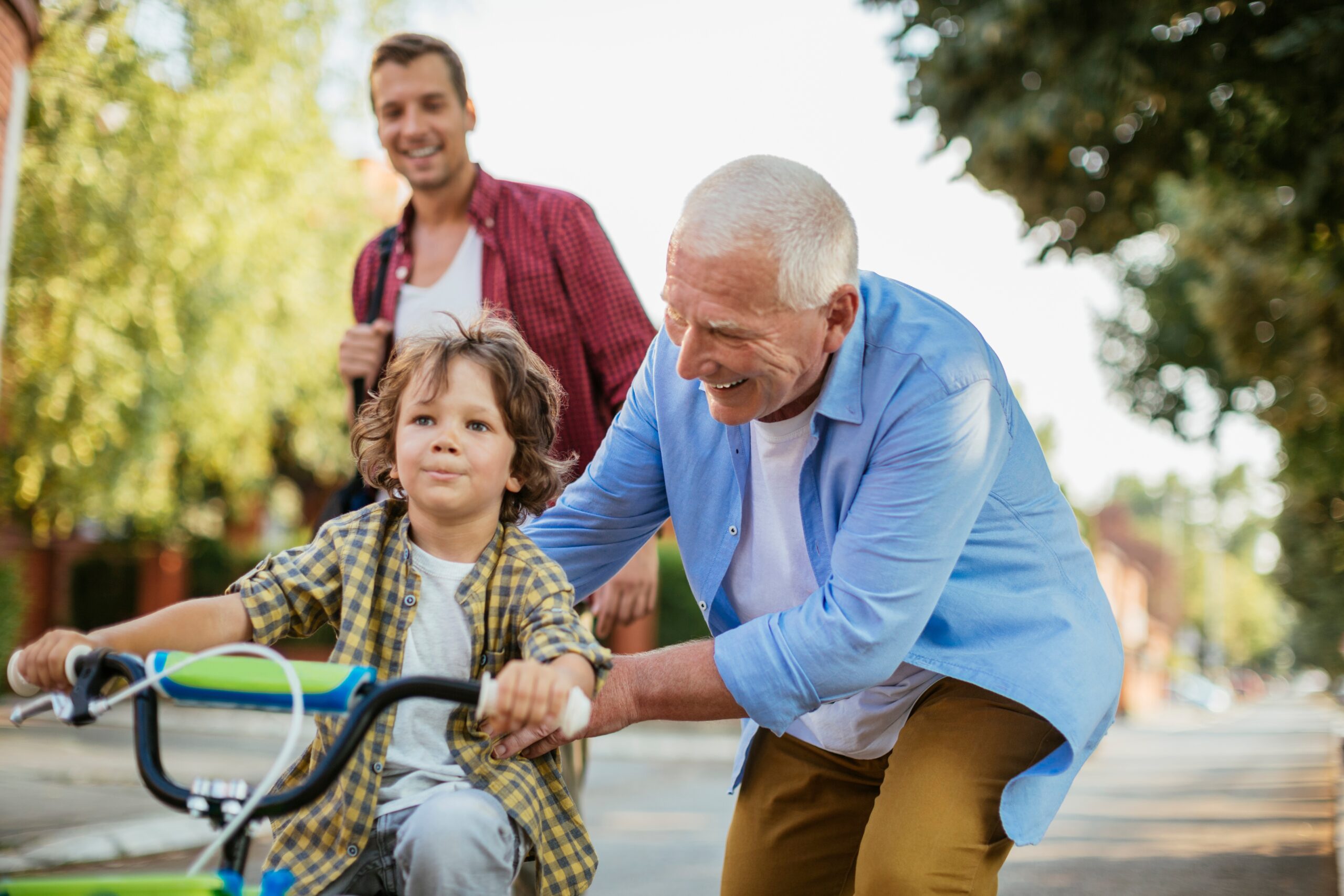 A father and grandfather teaching a young boy to ride his bike.