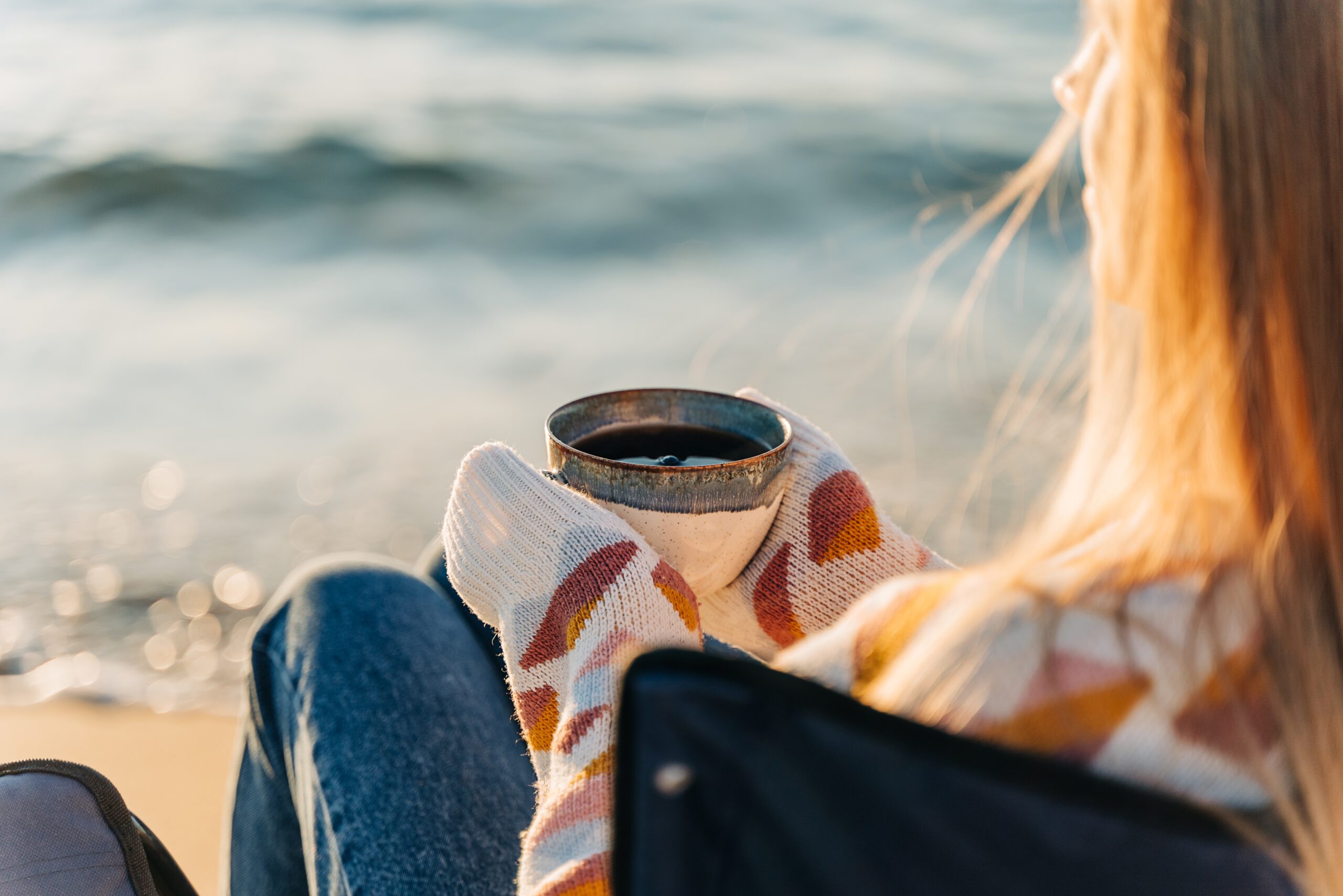A woman sitting alone in a chair on the sea shore.
