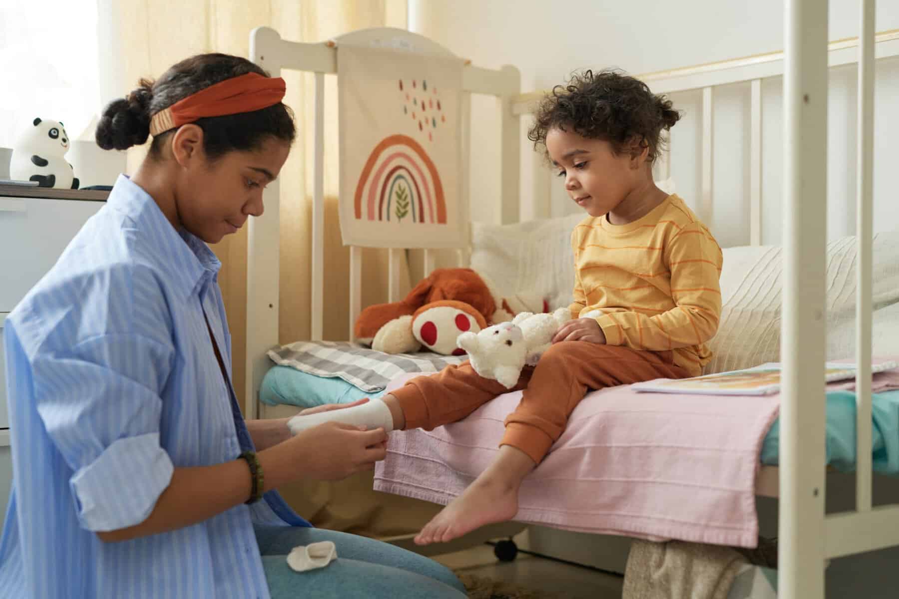 A caring older sister dressing a little girl in her nursery.