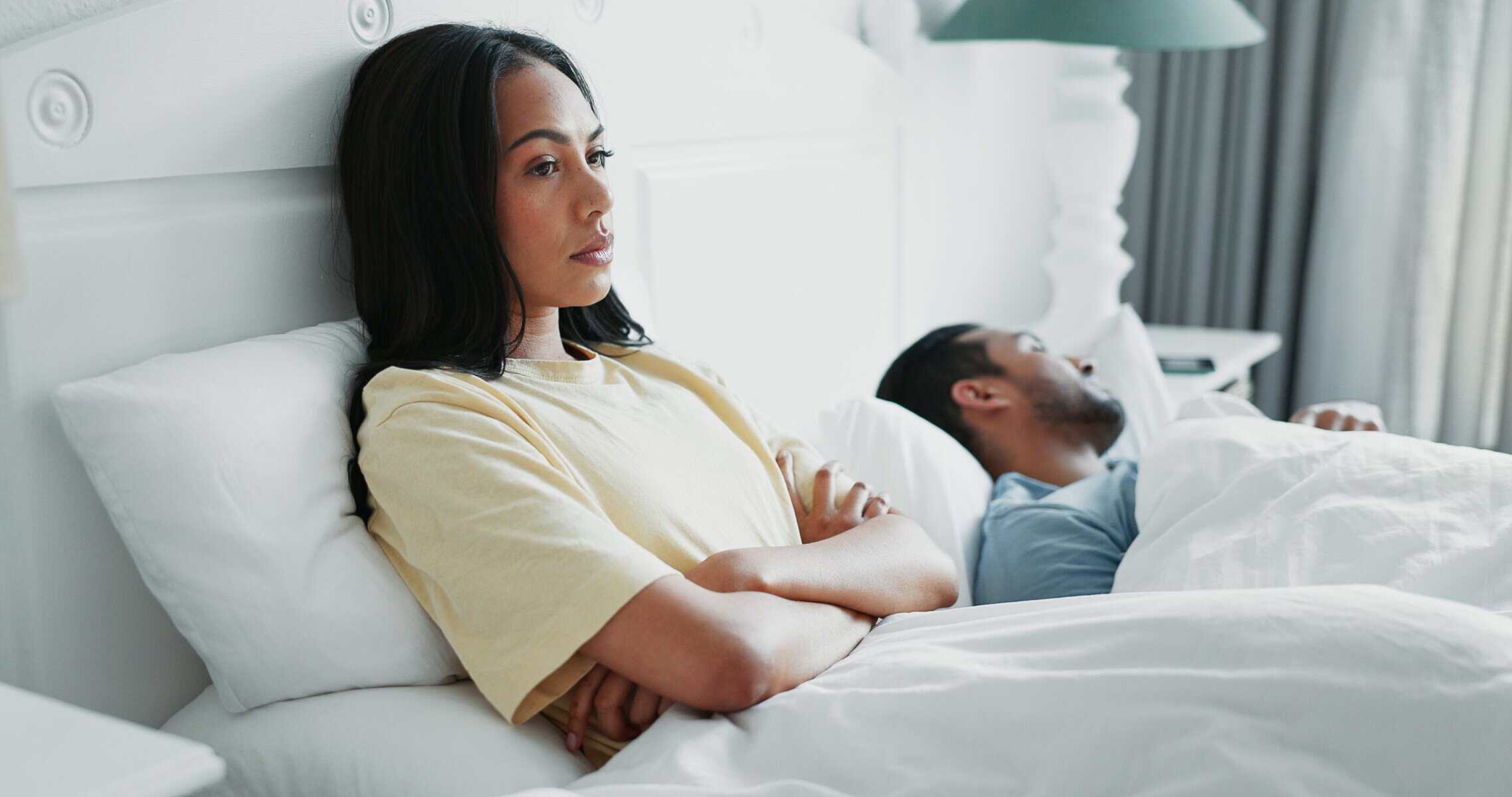 A woman laying upset in bed with her husband.