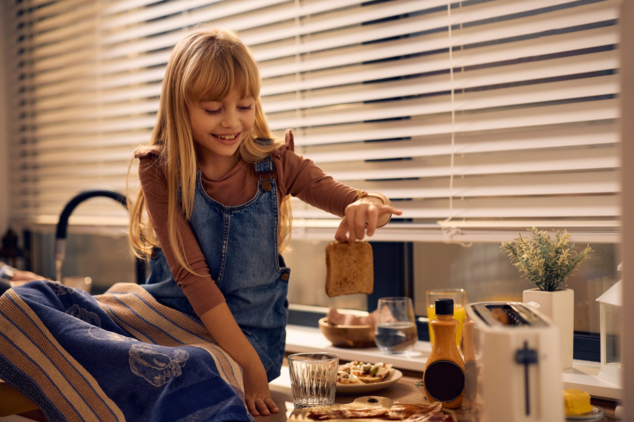 A little girl toasting bread while making a sandwich in the kitchen.