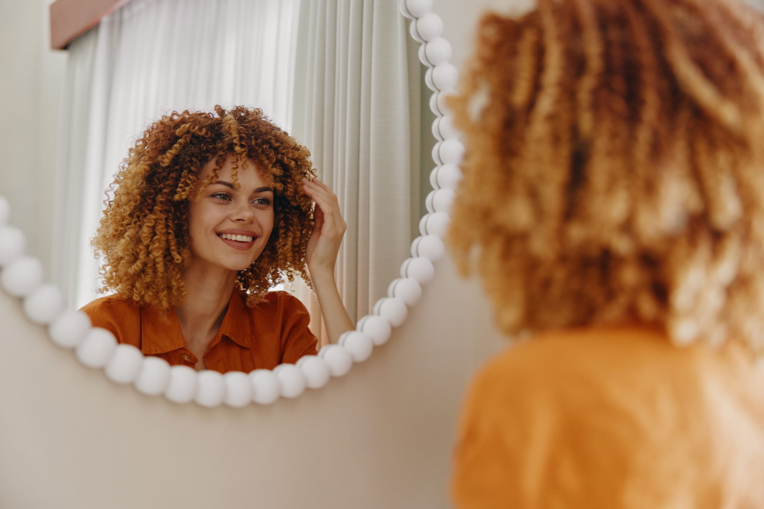 A woman is smiling confidently at her reflection in the mirror.