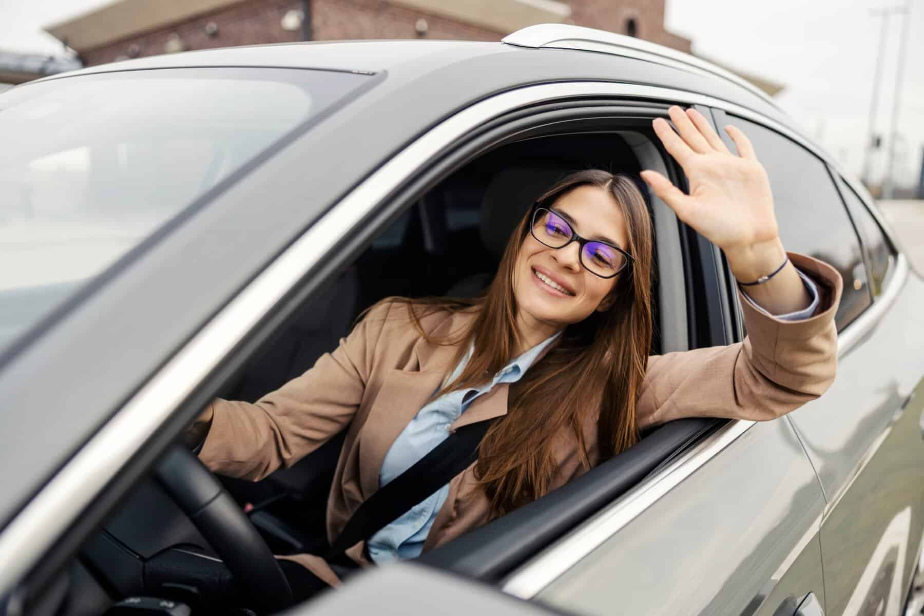 A polite female driver waving to other drivers in traffic.