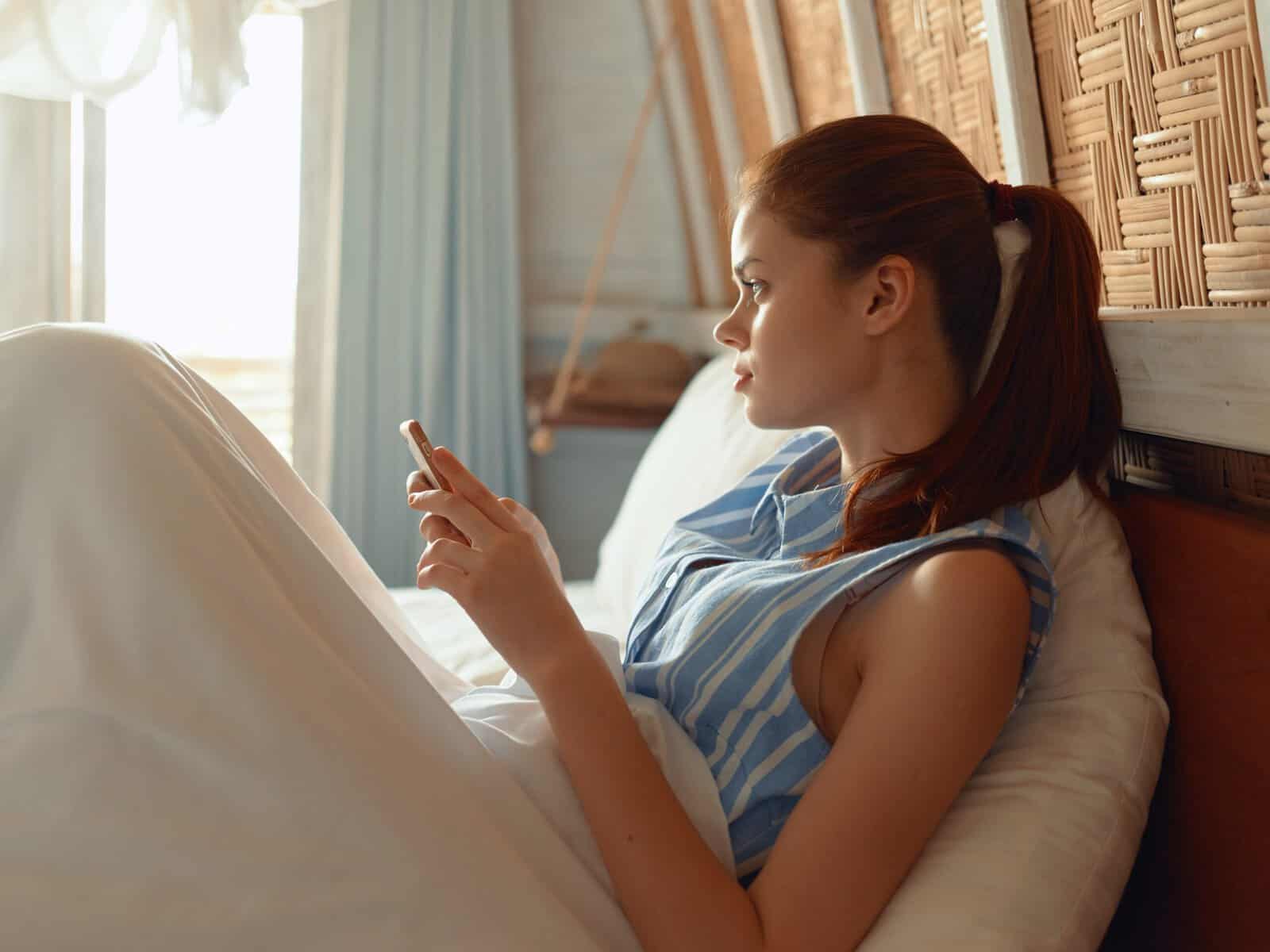 A woman laying in bed checking her phone for messages.