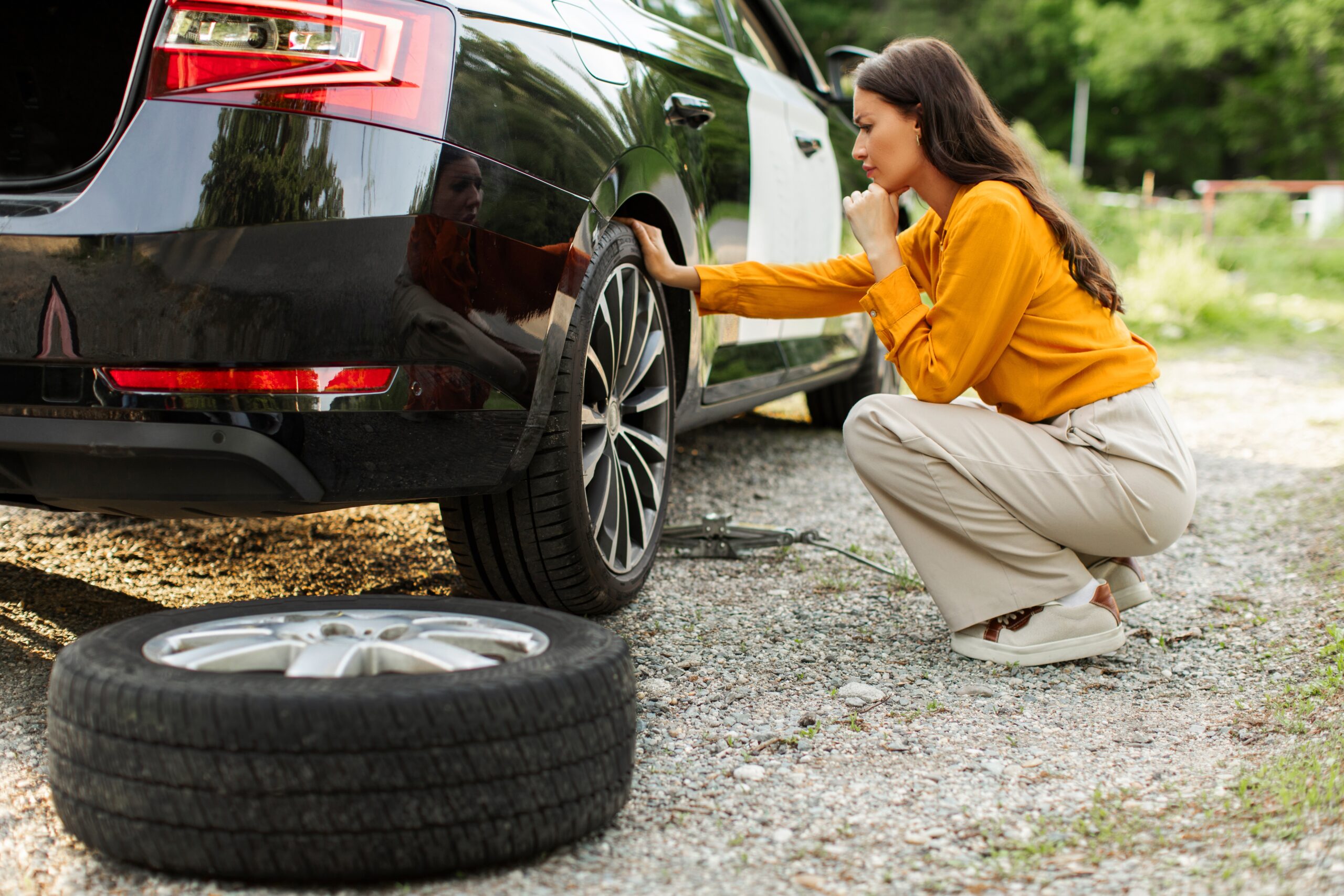 A stressed woman thinking how to change her flat tire.