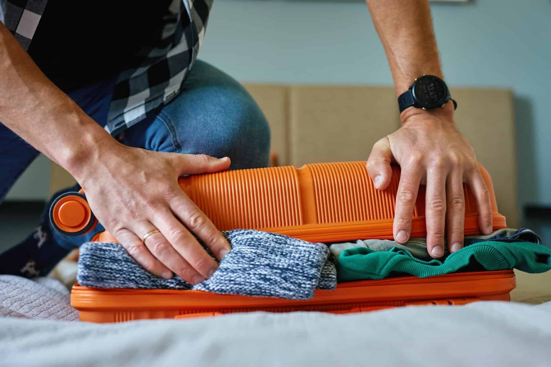 A man overstuffing his luggage for a trip.
