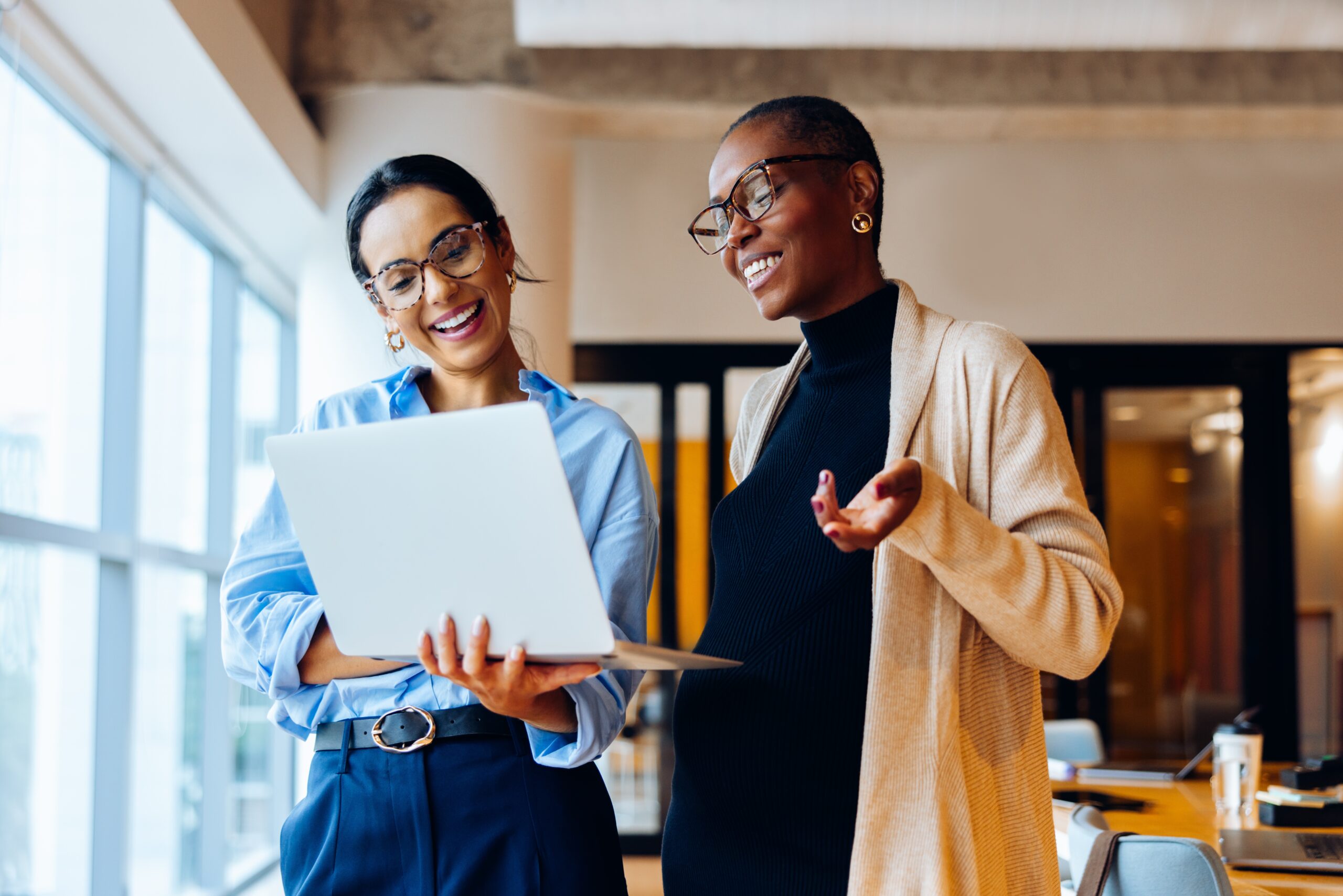 Two women in a professional setting sharing ideas and working on a laptop.