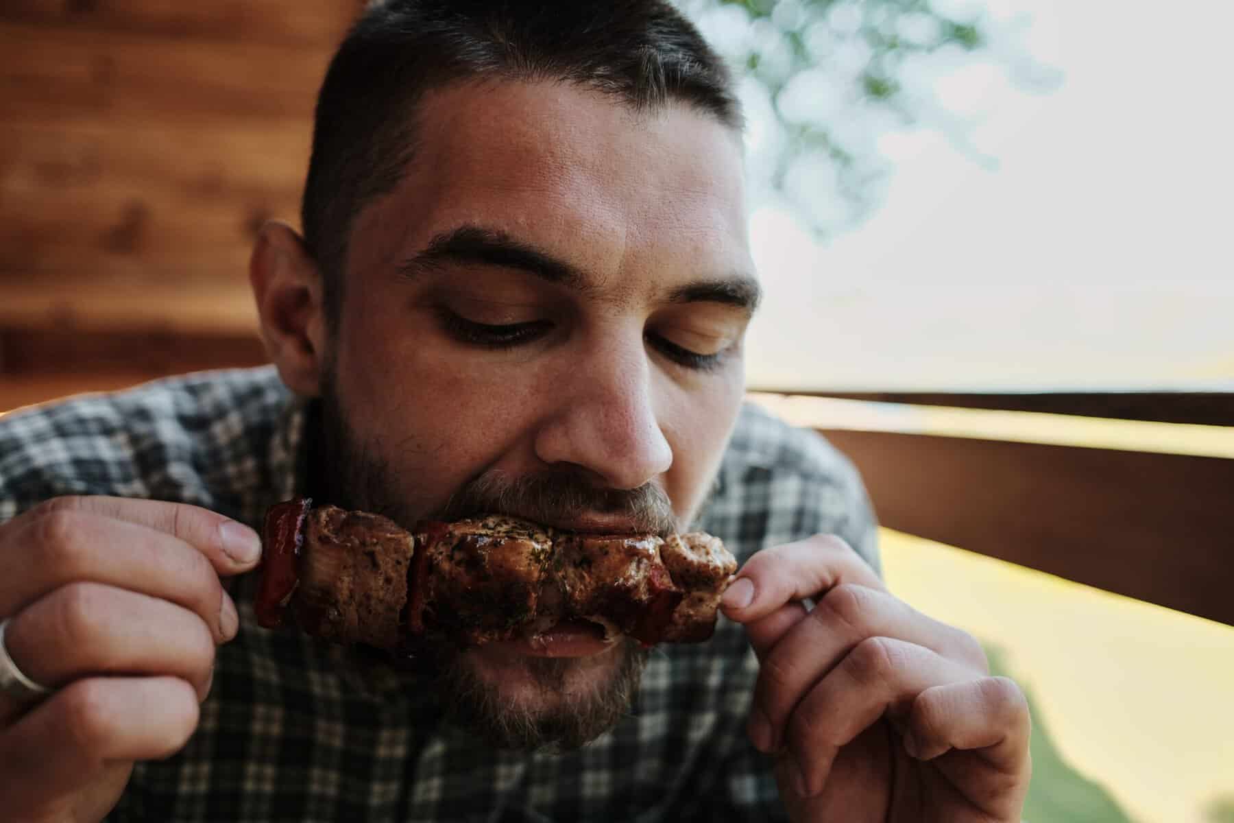 Man biting into a juicy grilled meat skewer.