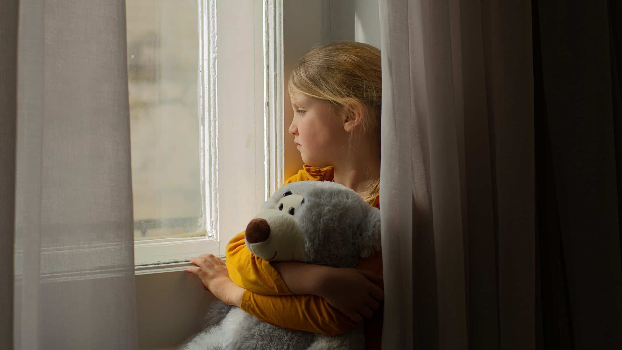 Sad little girl looking out the window.