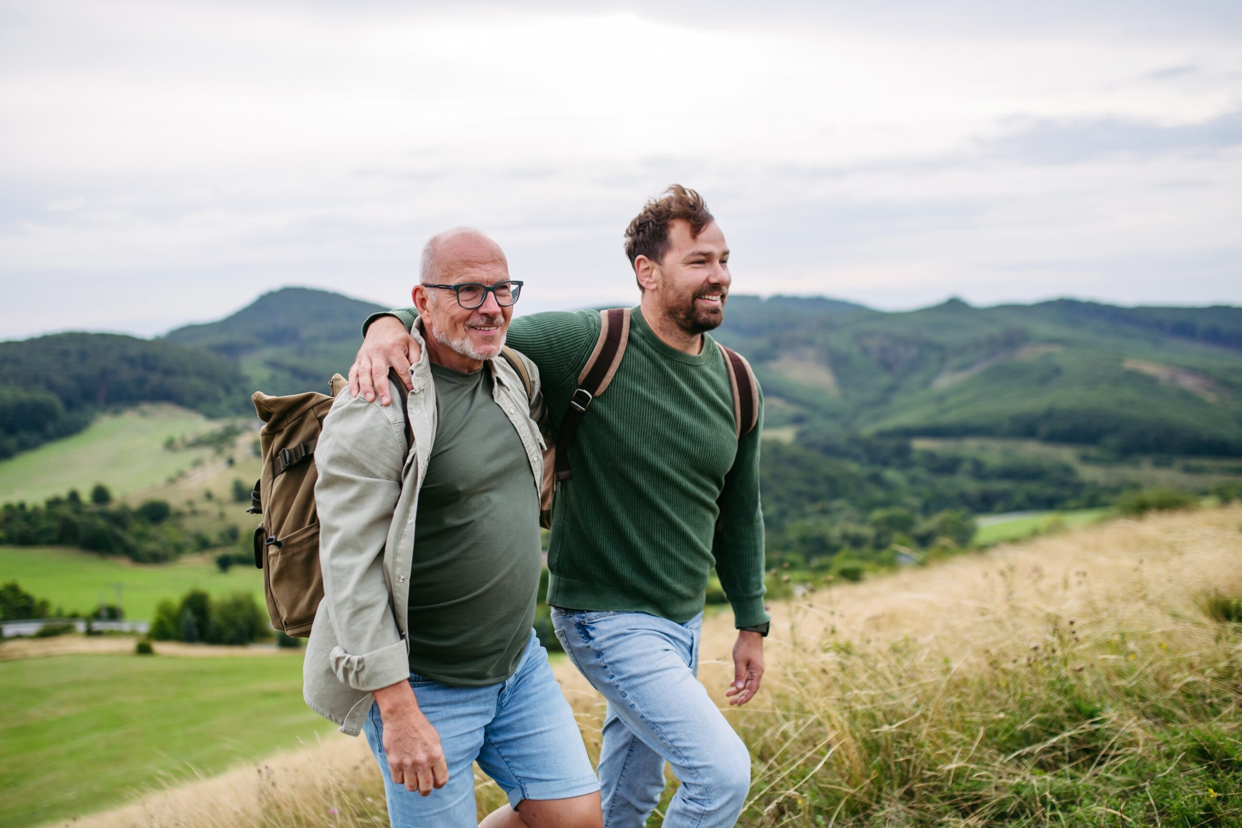 Adult son and older father hiking together in nature.