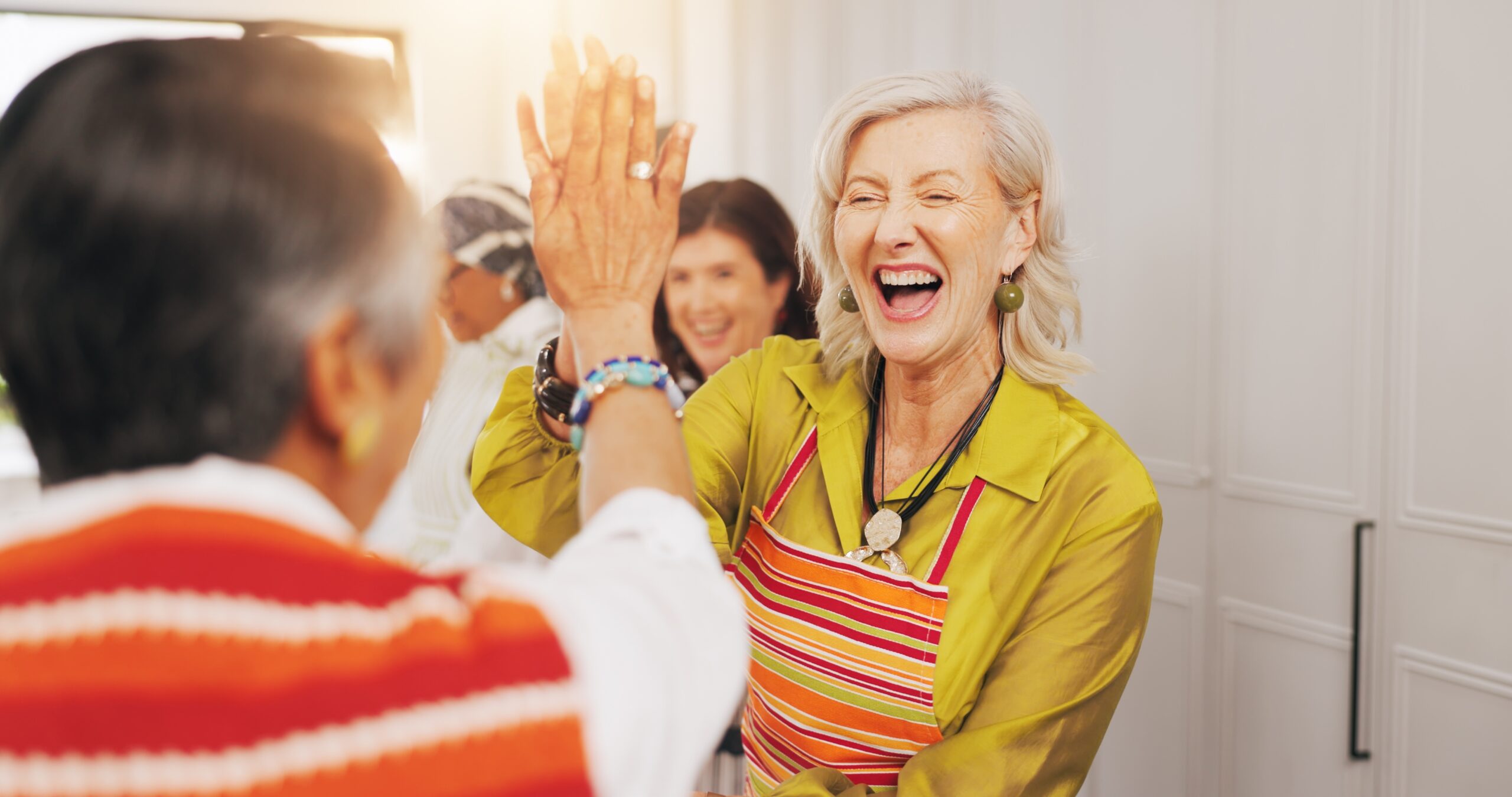 A cooking class with senior friends high five'ing in the kitchen.