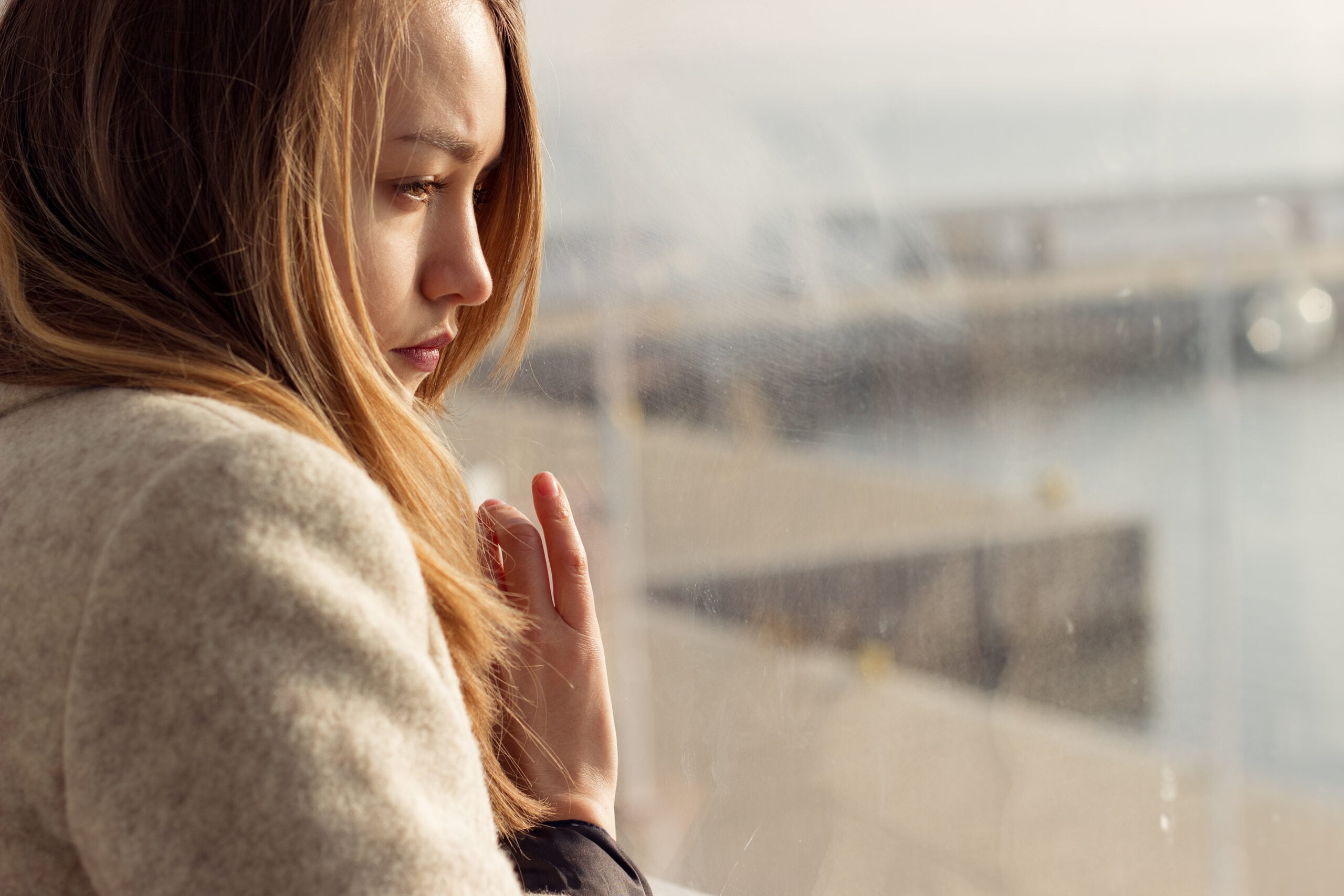 A lonely woman sitting near the window thinking about being alone.