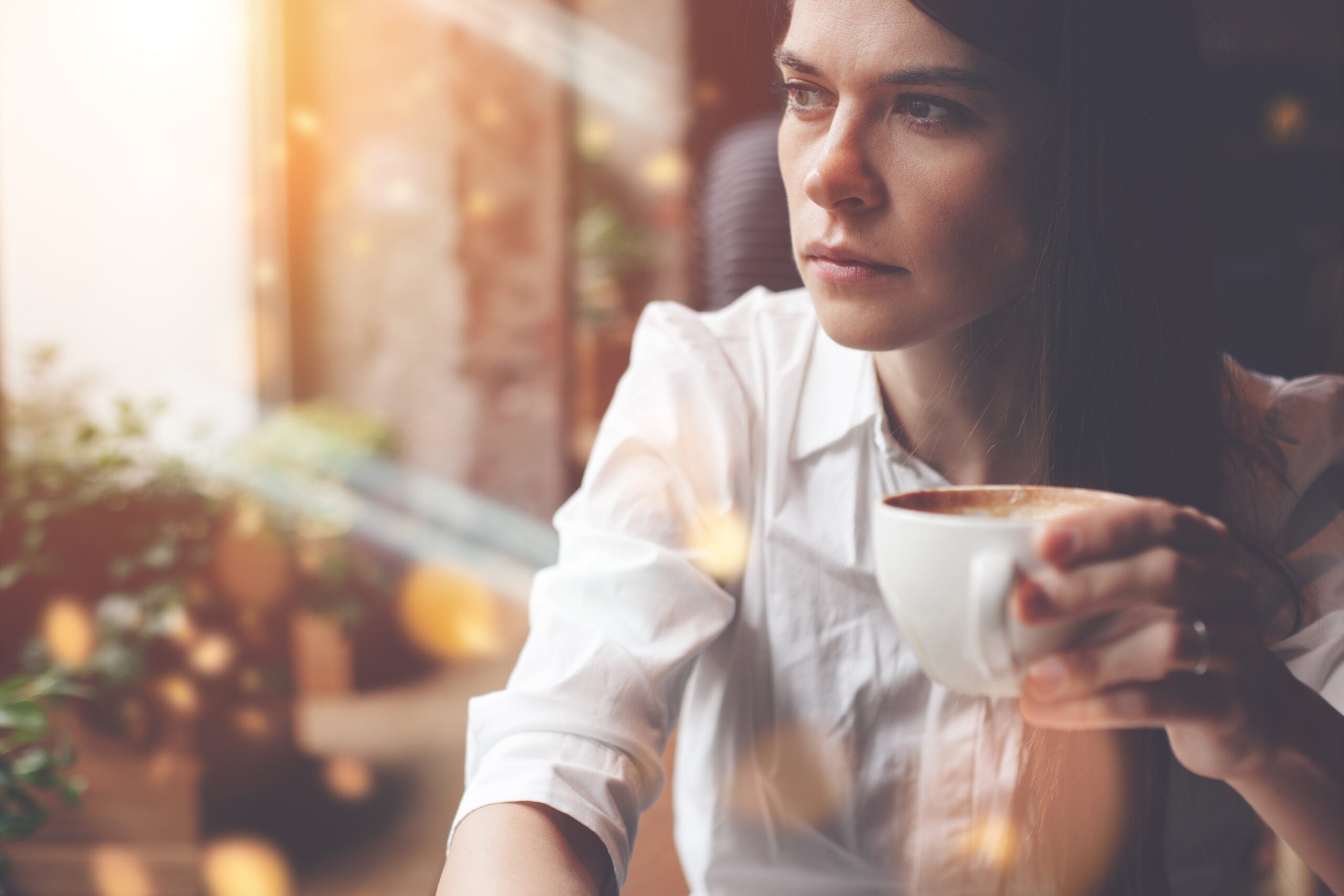 A lady sitting deep in thought with cup of coffee in a cafe.