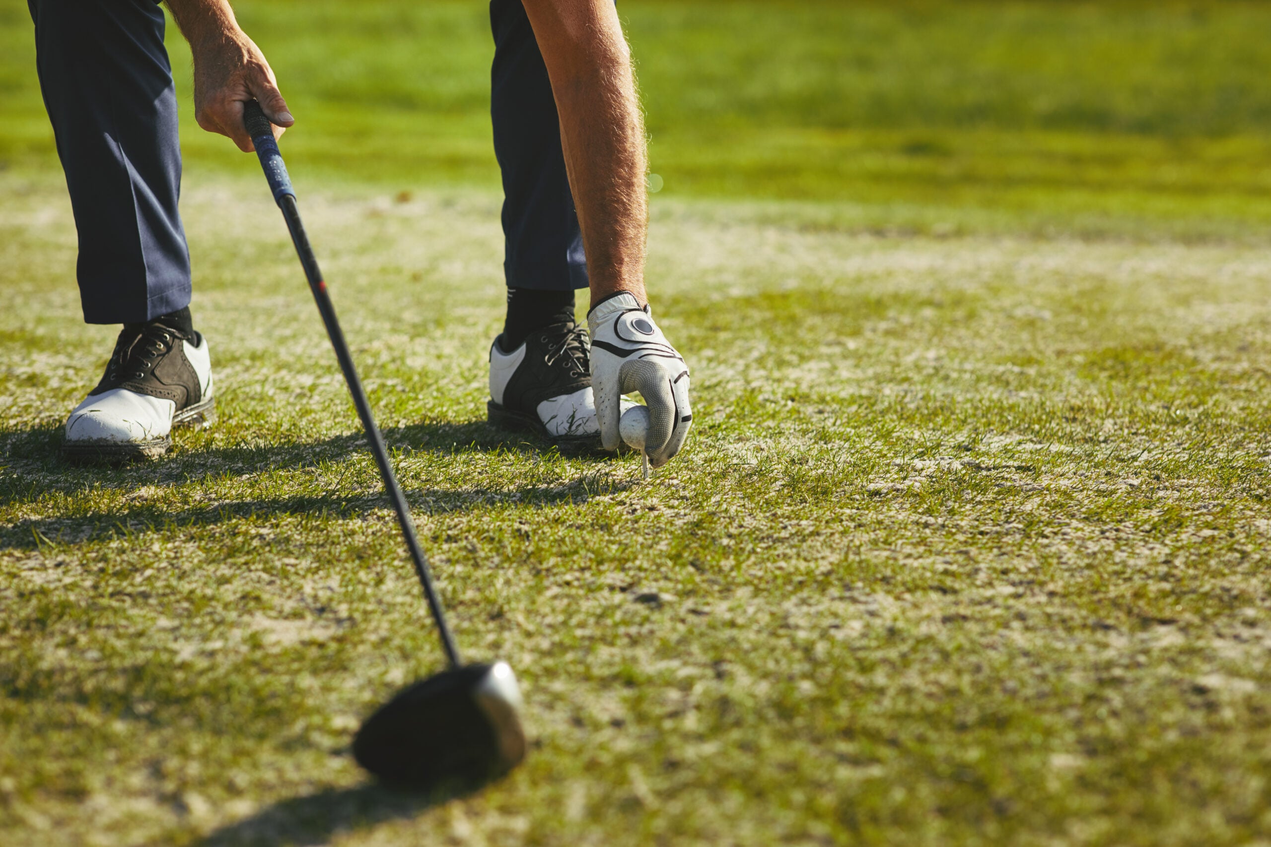 A retired senior man placing a golf ball on a tee on a sunny day.