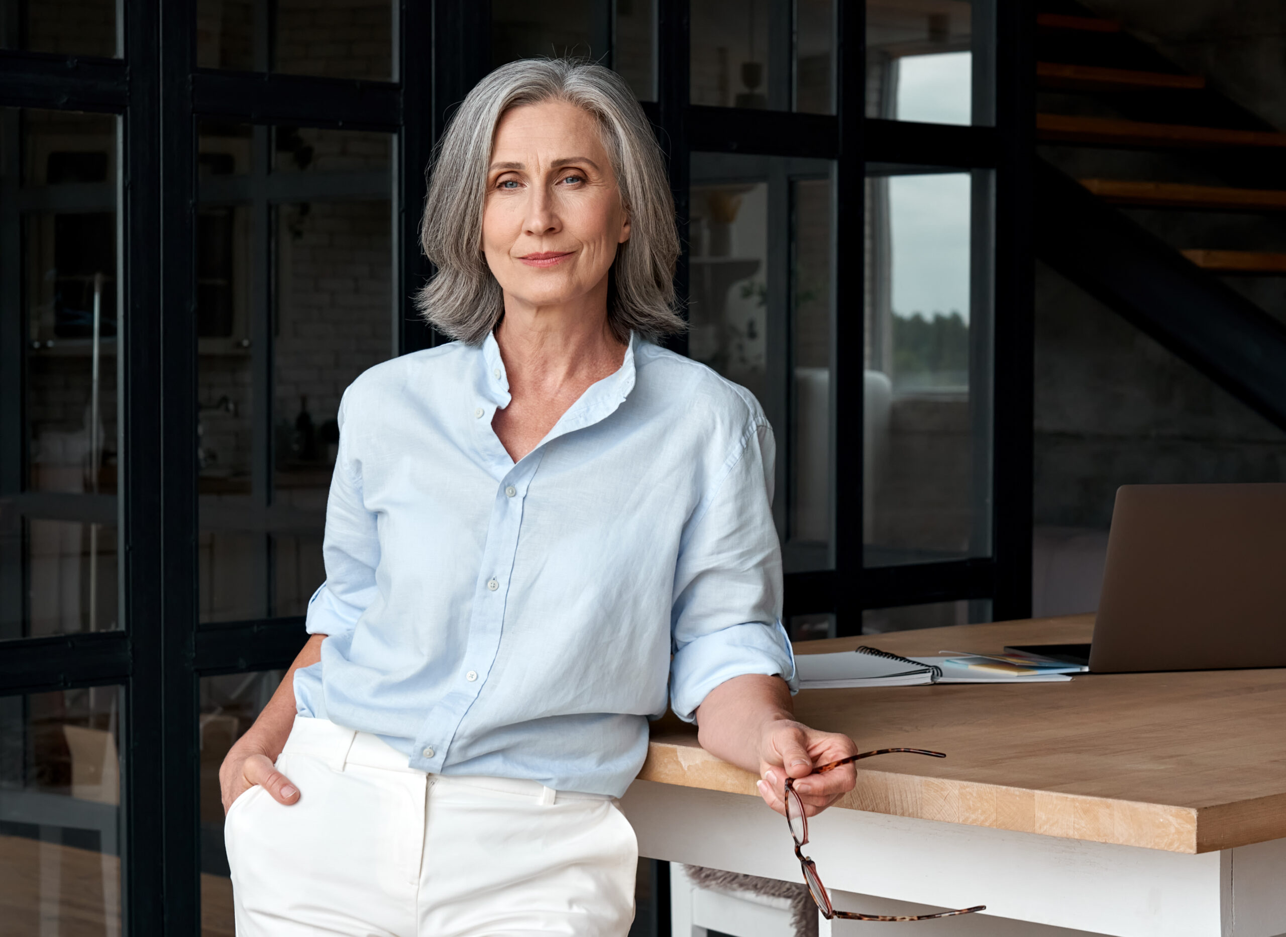 Confident older woman leaning on desk.