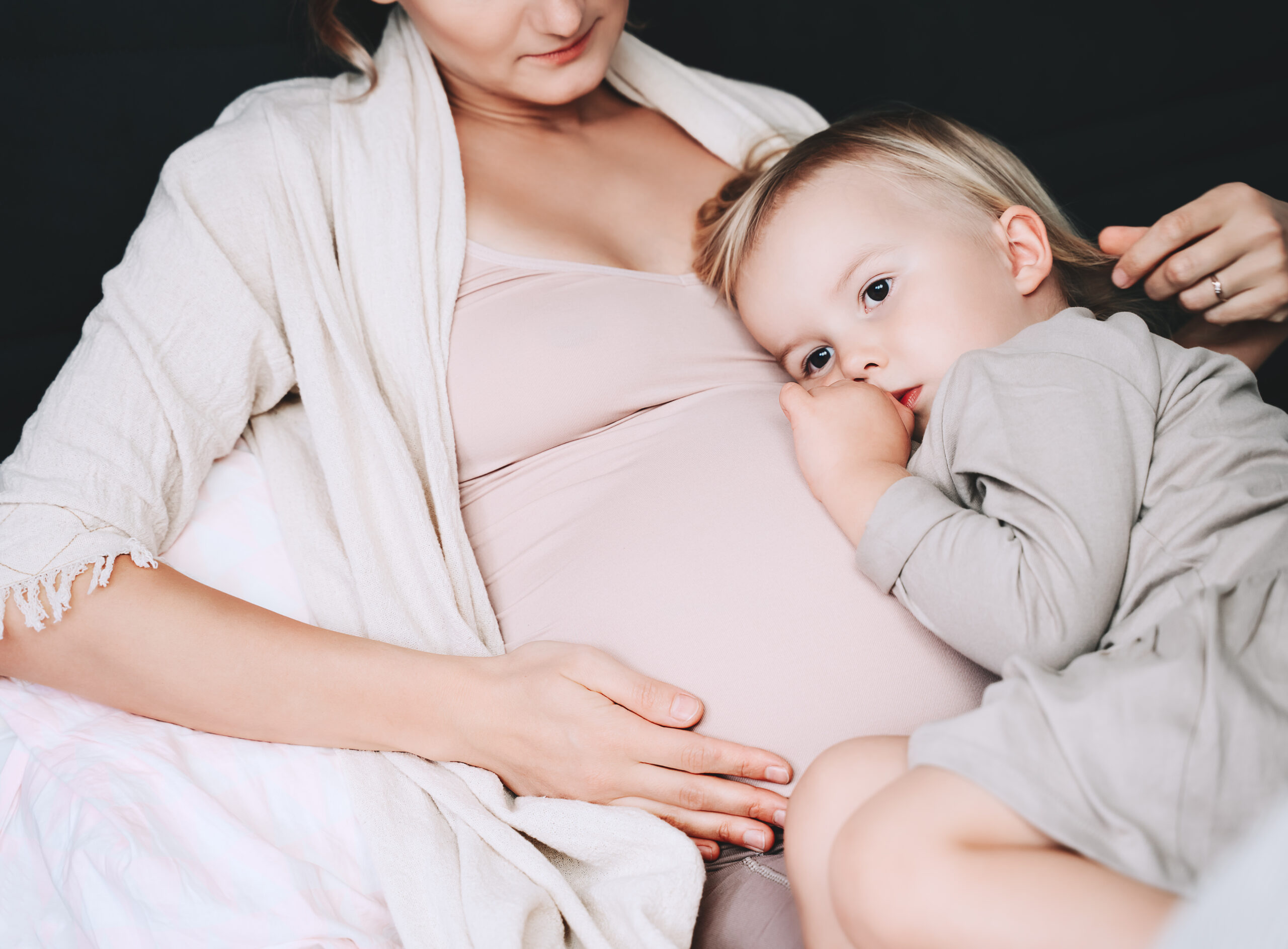 A pregnant mother with her toddler daughter laying in bed.