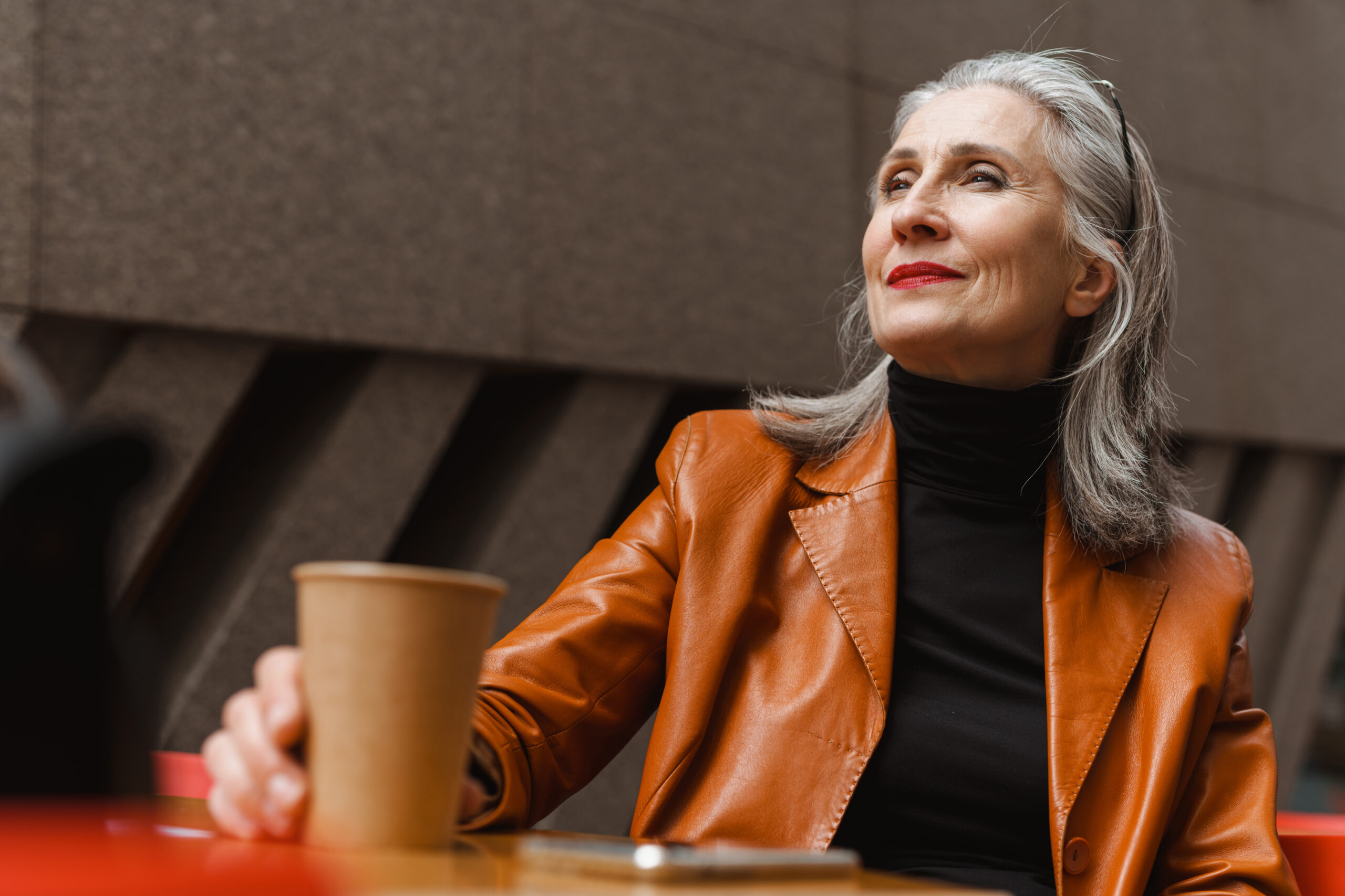 A senior woman drinking coffee while sitting in an outdoor cafe.