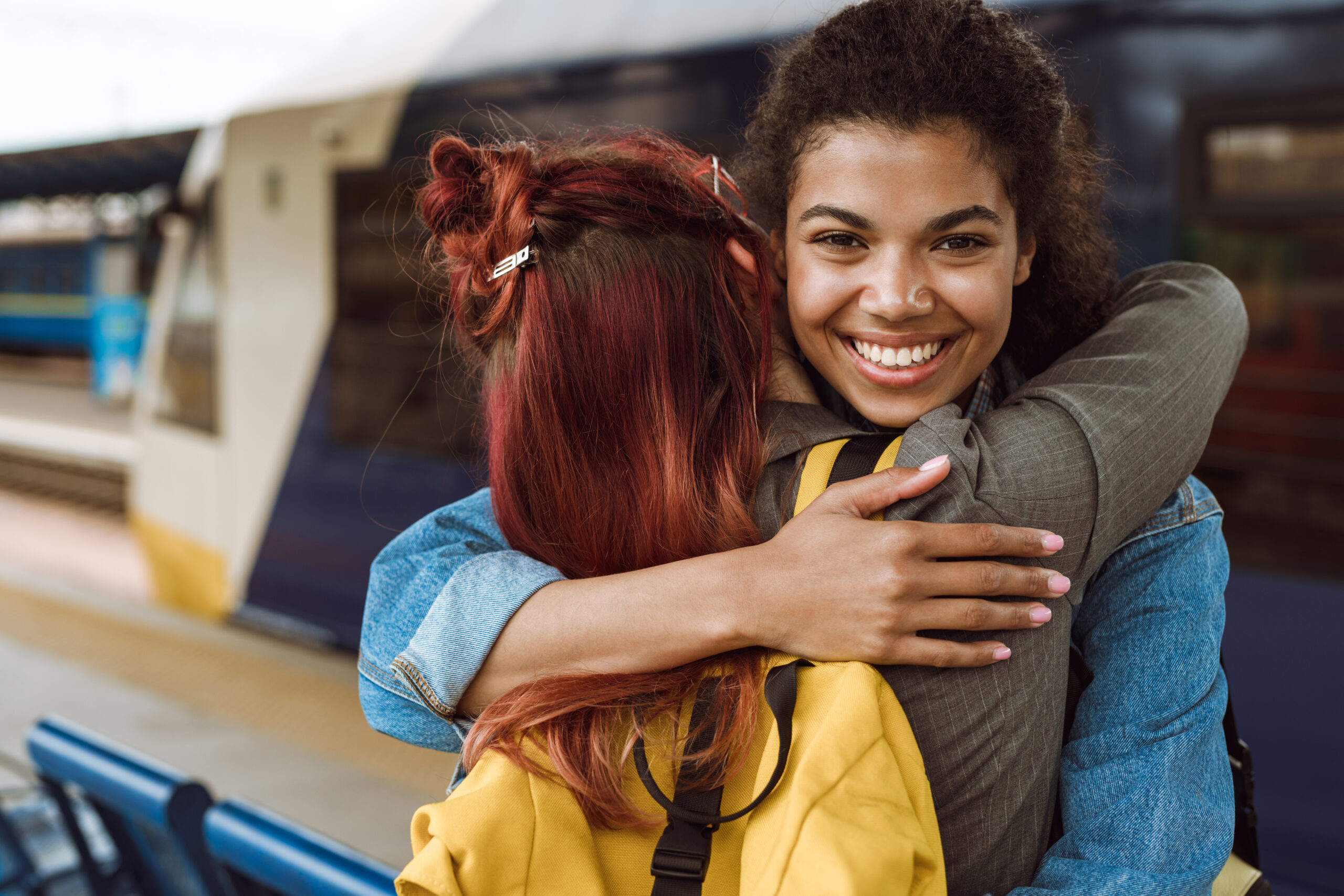 Two women smiling while hugging goodbye at the train station.