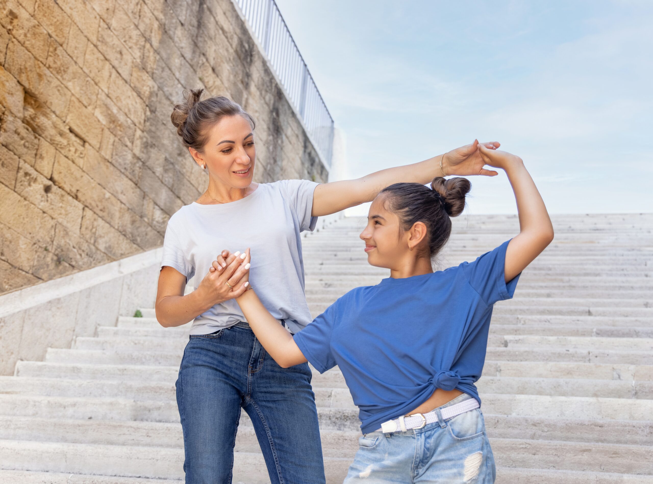 A middle-aged mother and her happy daughter standing on stairs outdoors.