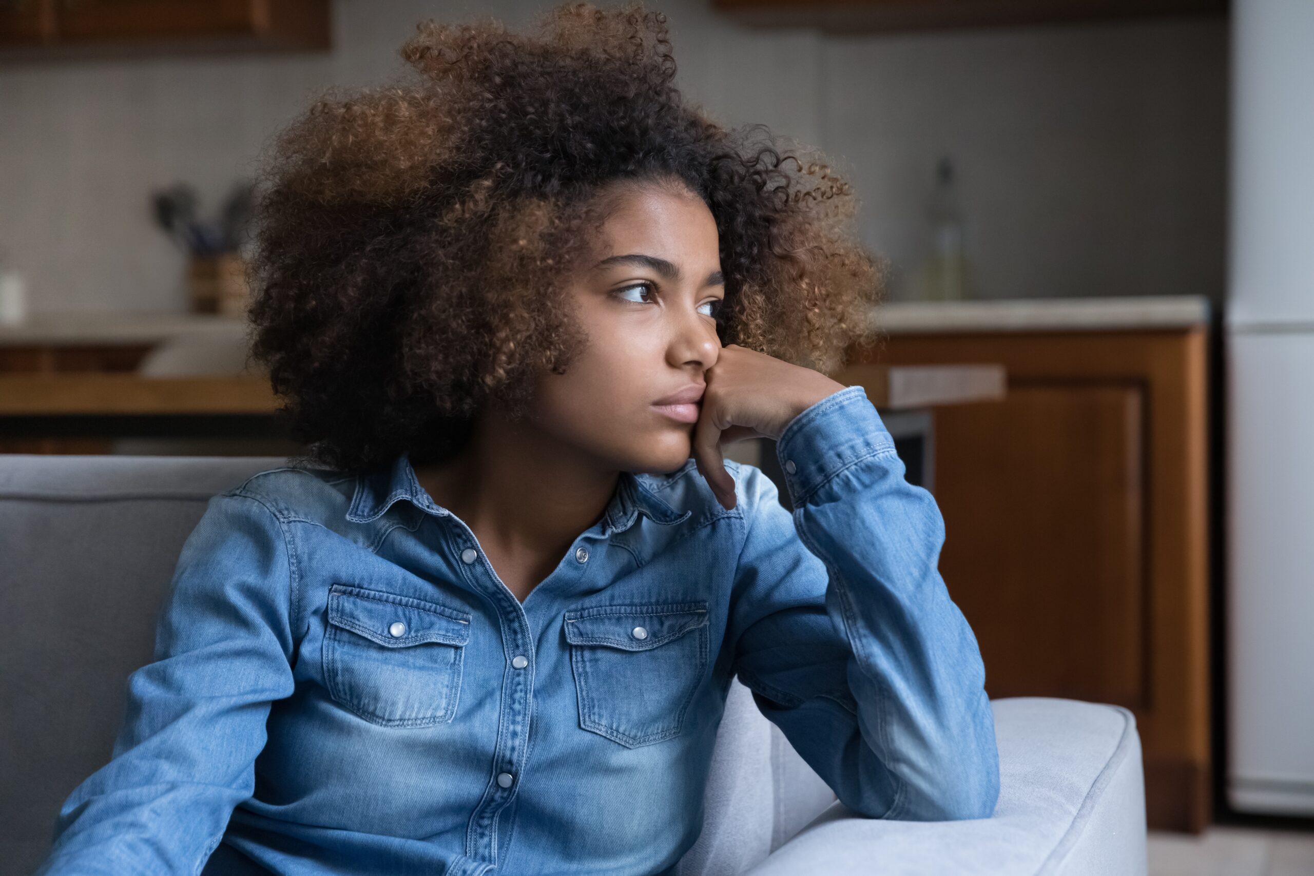 A frustrated teenage girl sitting on the couch at home.