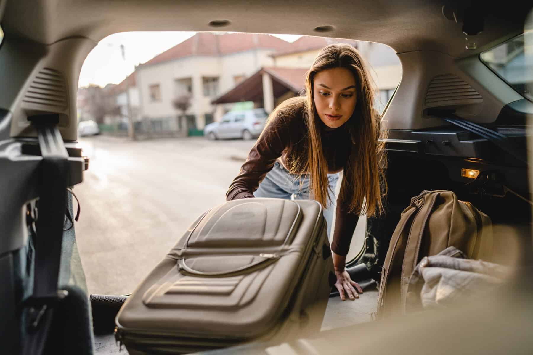 A woman packing up her suitcase in her car.