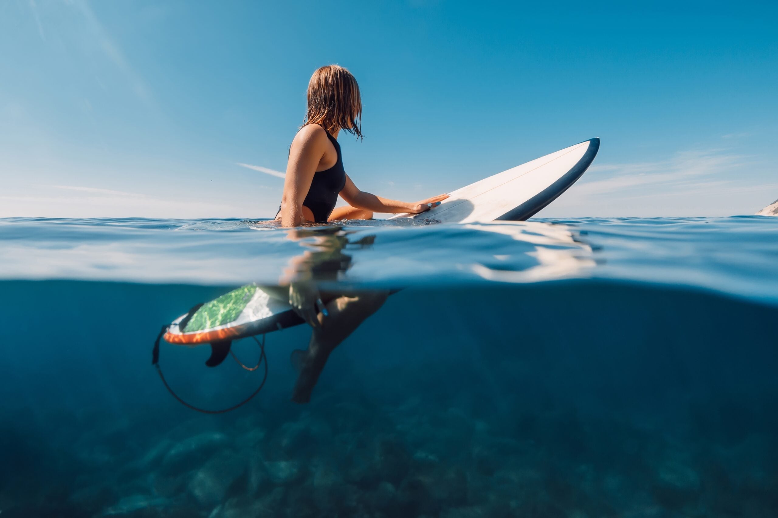 An independent surfer girl sitting on surfboard in the ocean.