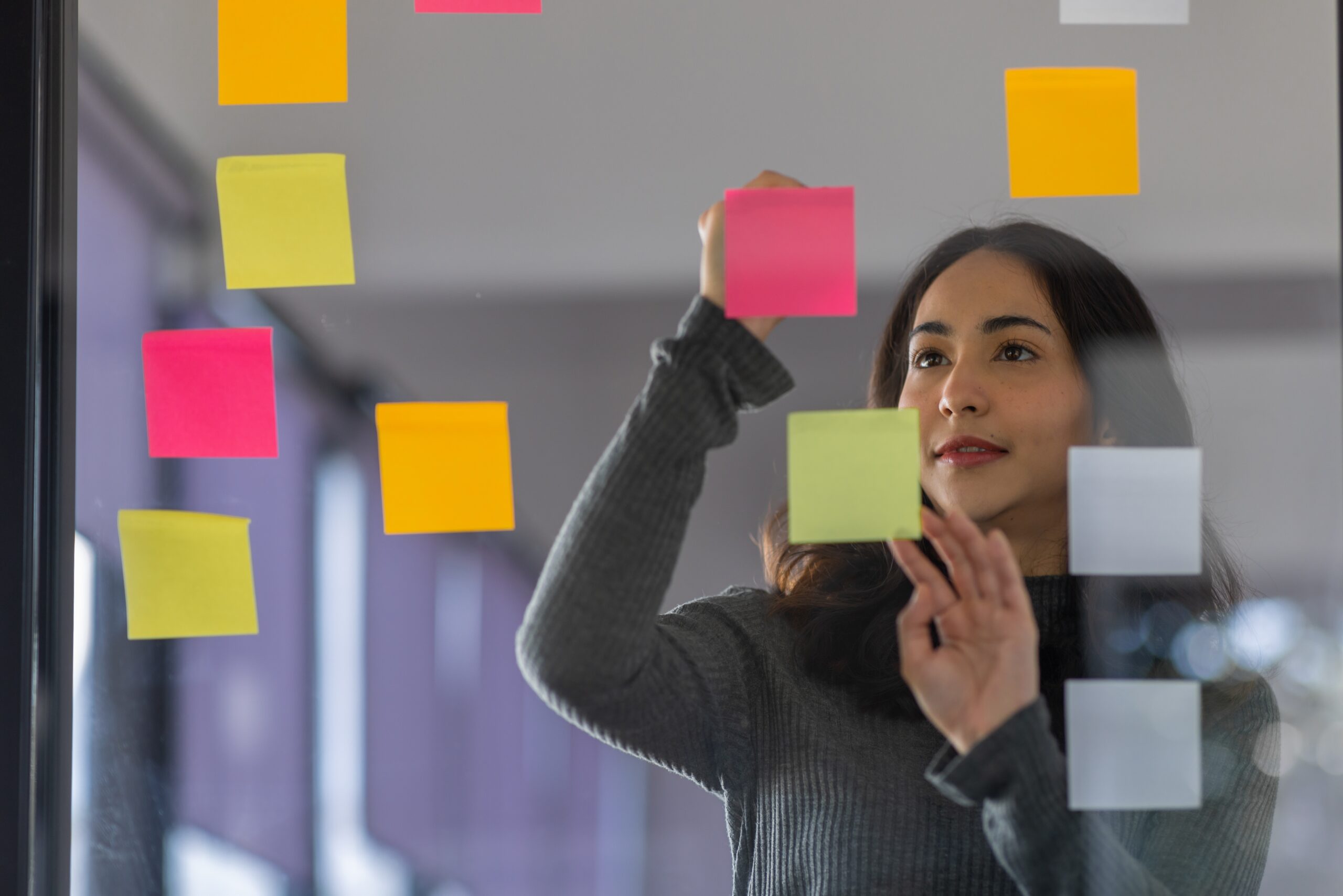 Woman organizing post-its on a glass wall.