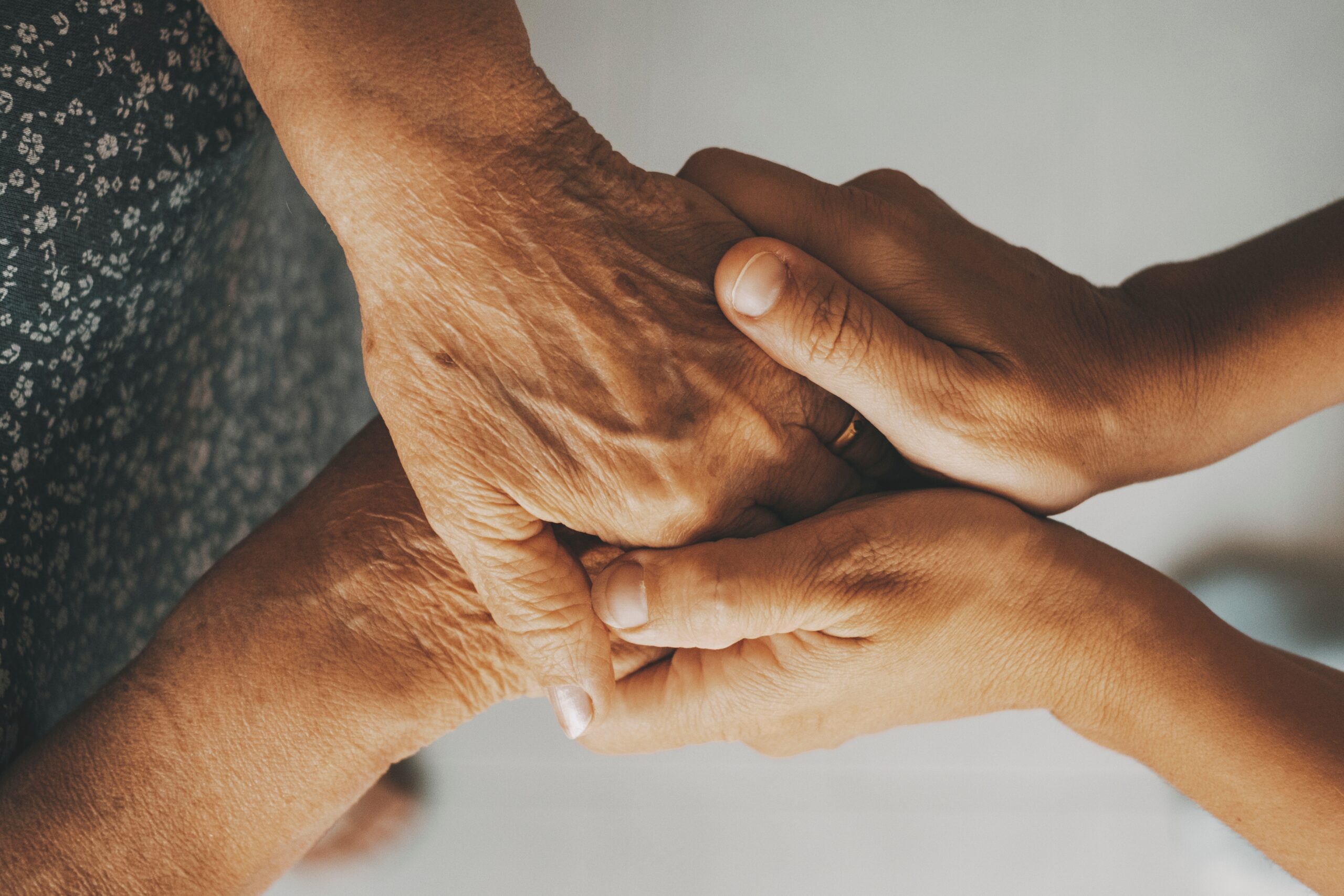 An adult son holding the hands of his senior mother.