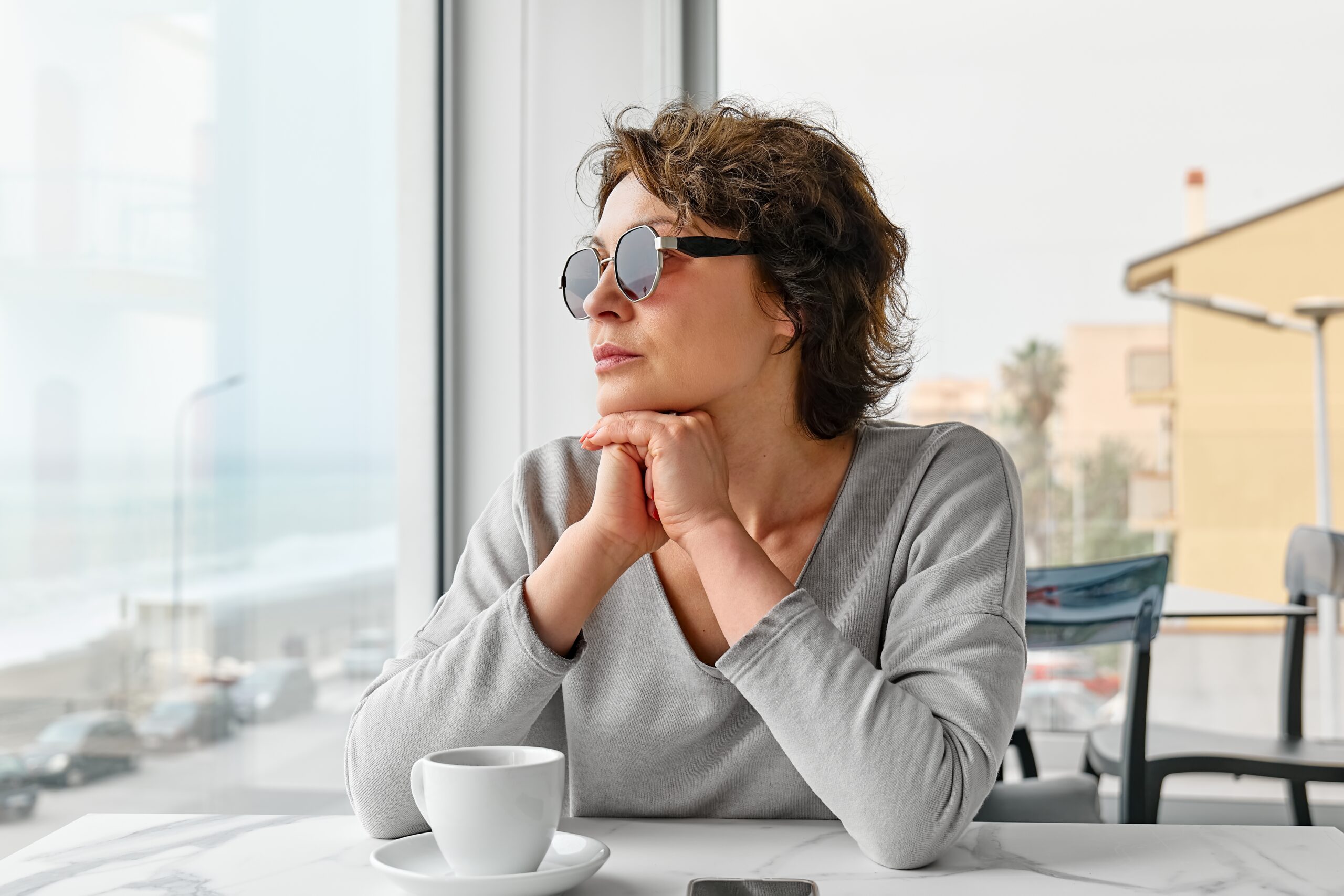Confident woman looking out the window while having coffee alone.